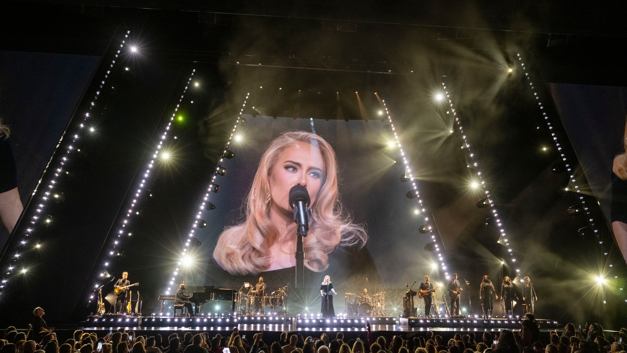 Singer Adele performing on stage in front of crowd band members cover the stage and Adele's performers is projected on a huge LED screen