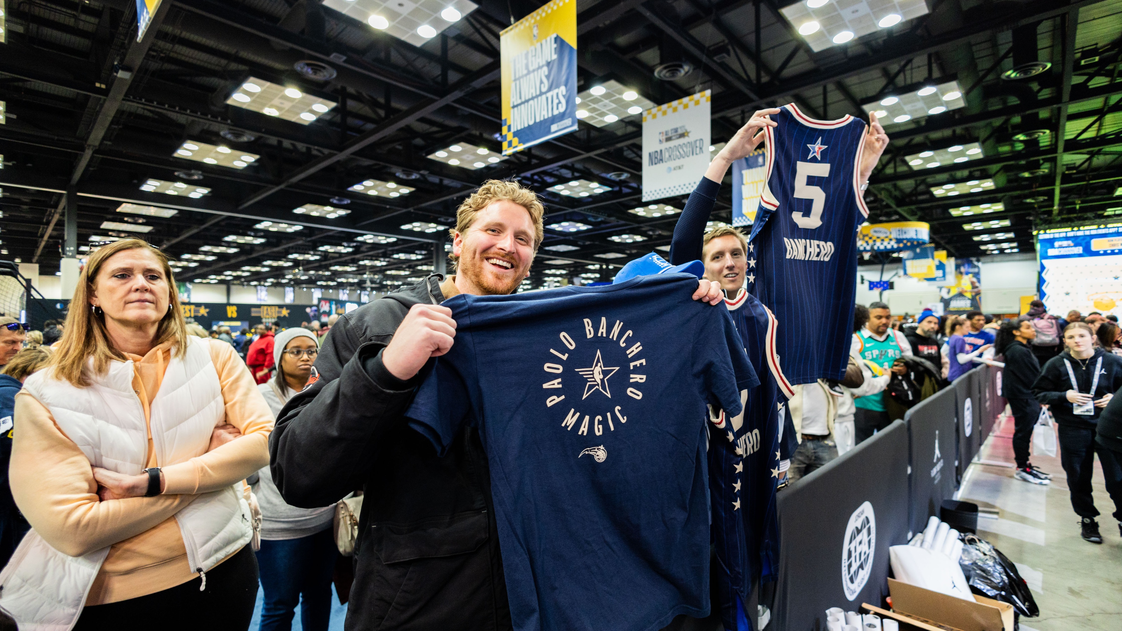 2 men holding up sorts jerseys at a brand activation