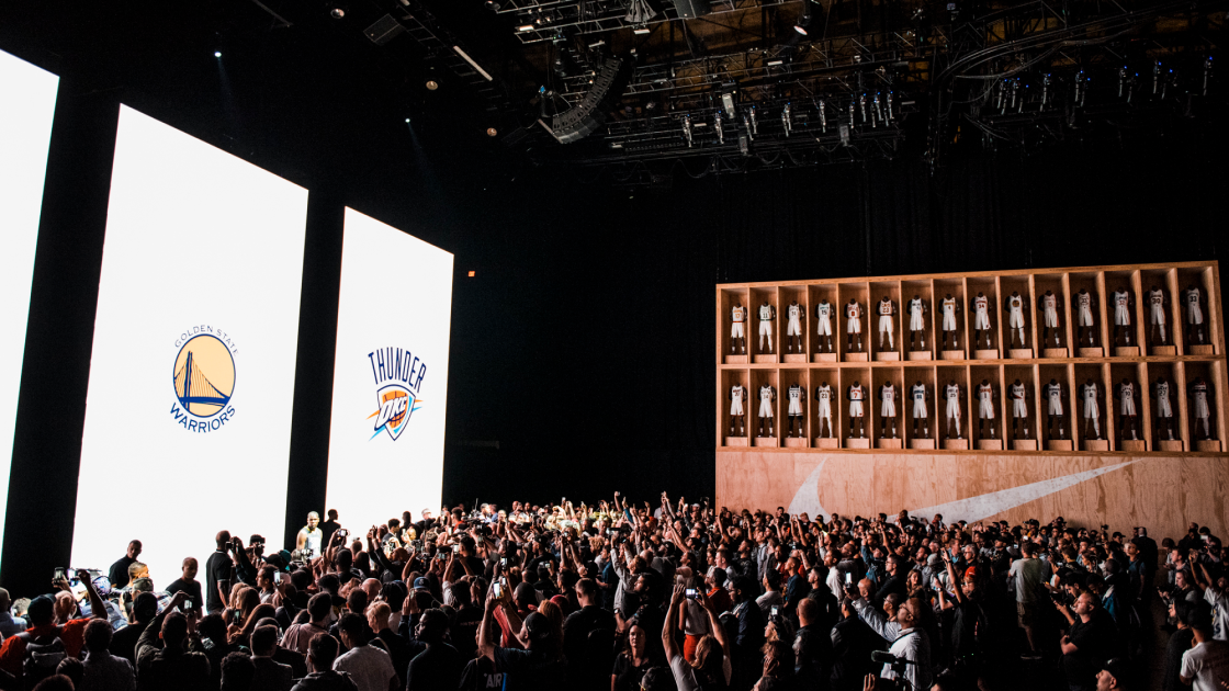 image of audience in front of Nike uniform display and 3 large vertical screens