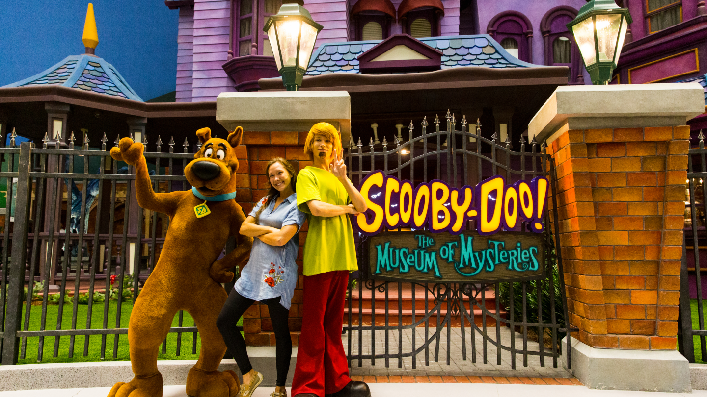 Scooby Doo and Shaggy posing for photo with guest in between them in front of Scooby-Doo The Museum of Mysteries