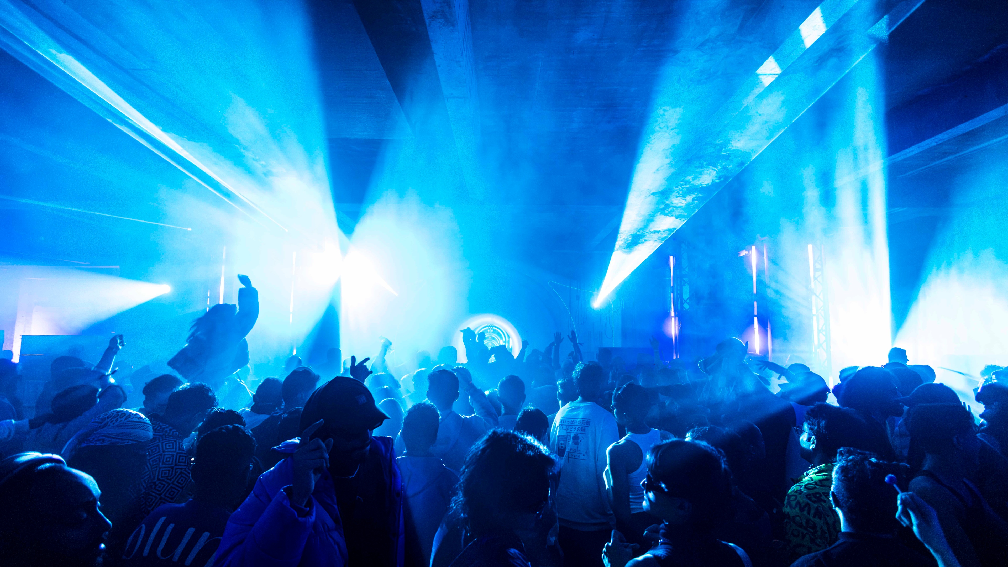 Crowd of people dancing to DJ set in dark room with blue strobe lights and smoke