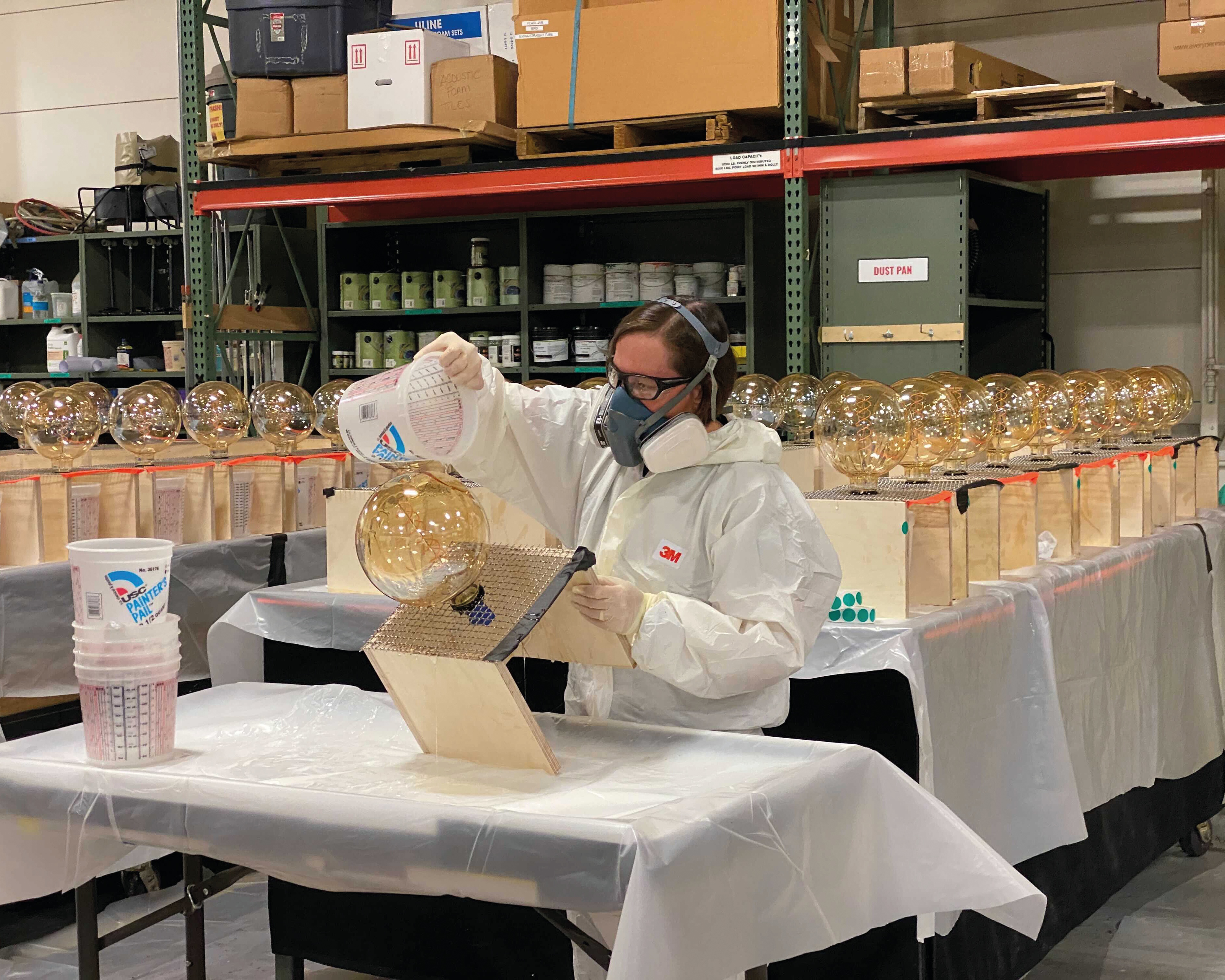 Woman in safety attire, googles, and mask, dyeing glass lamps for the Black Crowes Shake Your Money Maker Tour