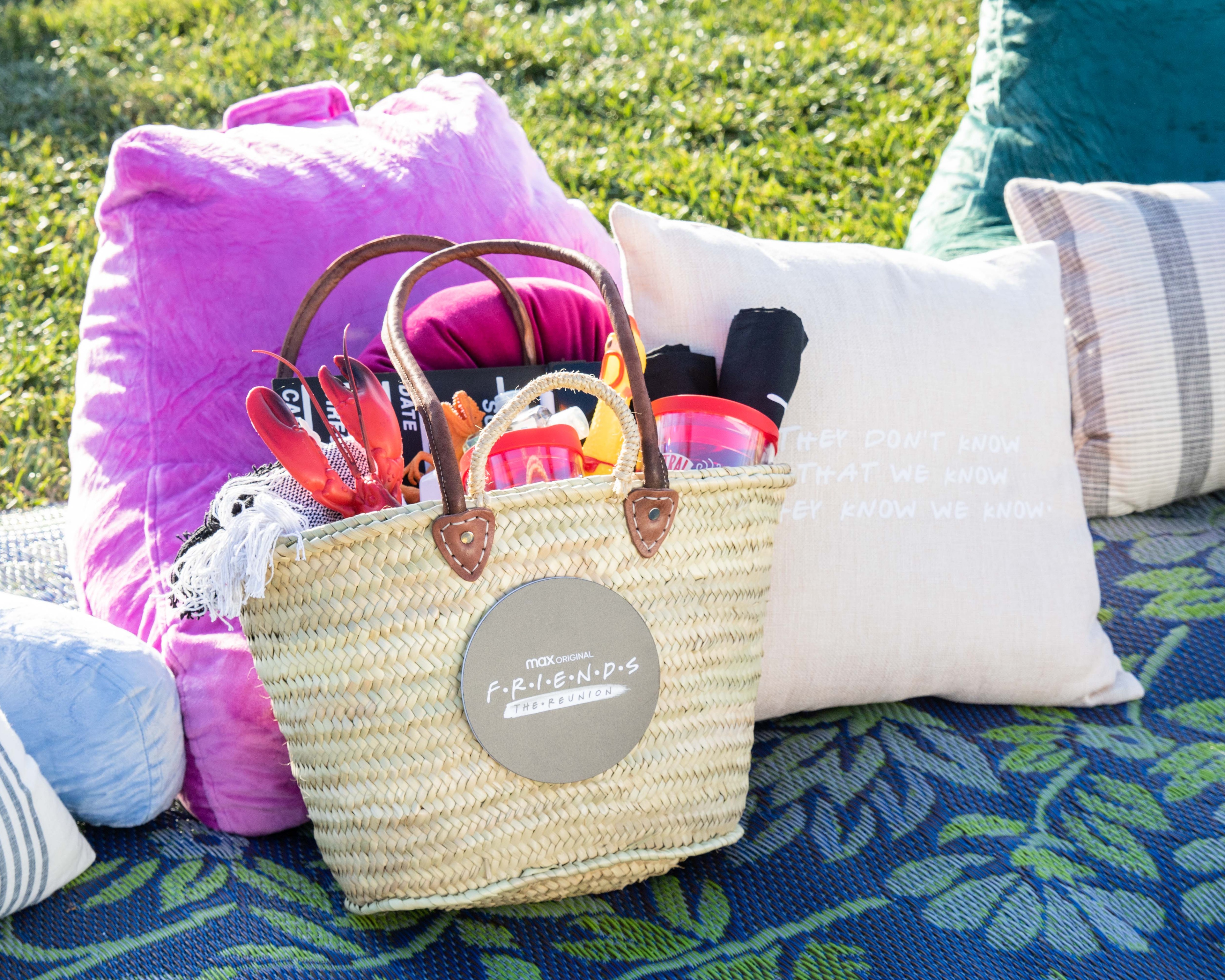 Gift bag with Friends logo on it laying on floral blanket and cushions on field