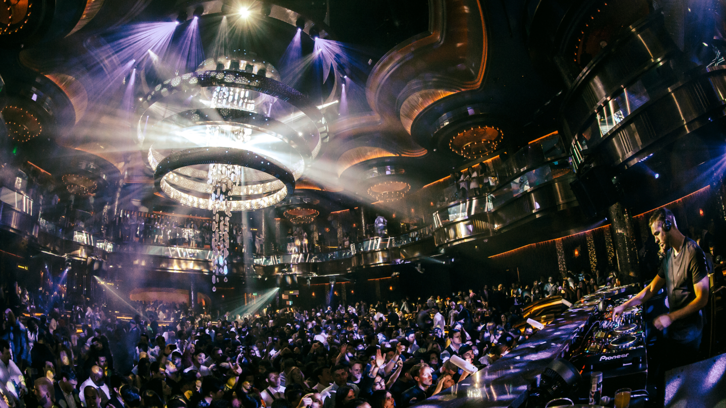 crowd dancing in club being lit by chandelier with dj playing music