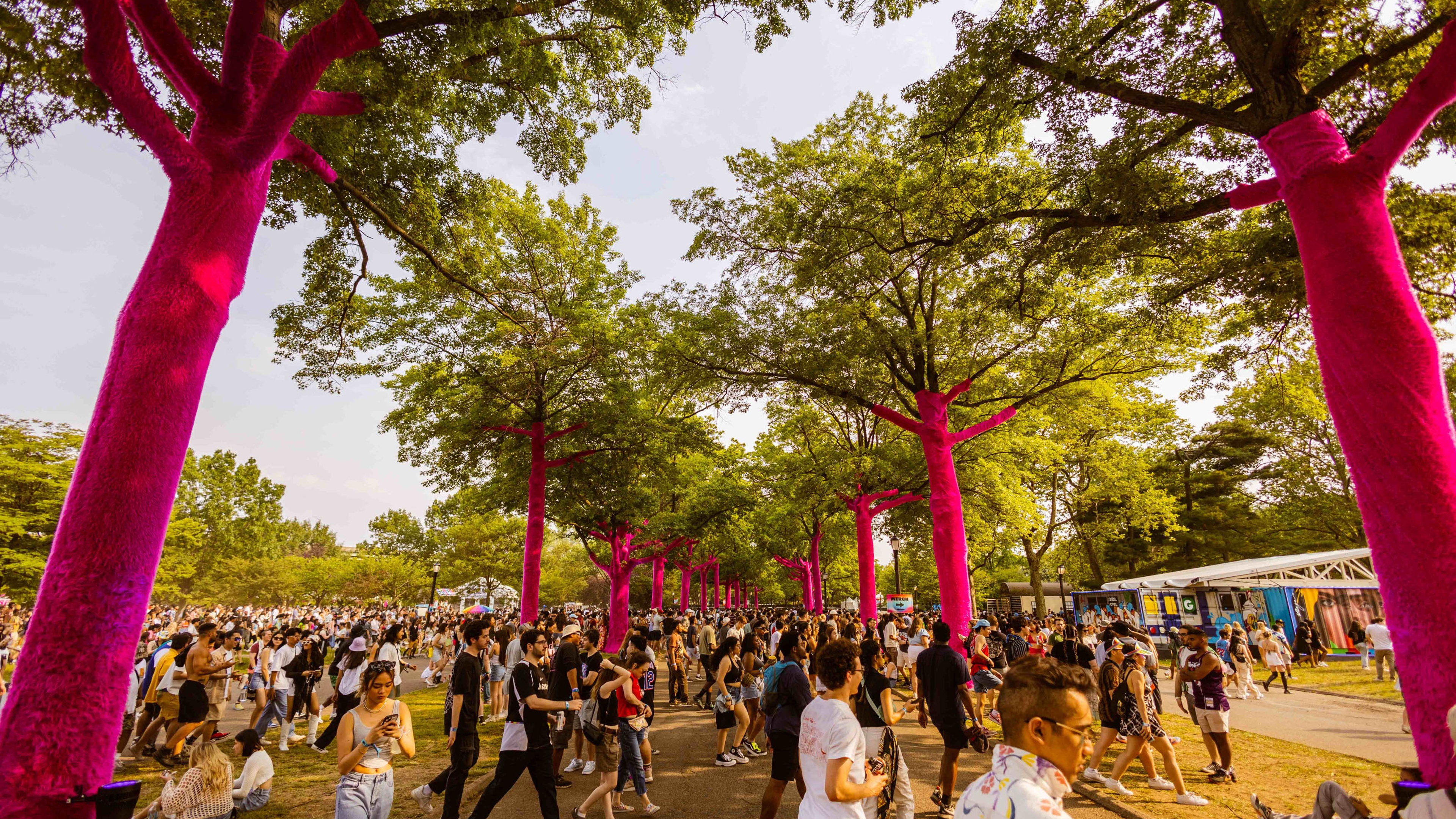 Founders Entertainment The Governors Ball crowd walking across a pathway flanked by trees wrapped in bright soft magenta fake fur