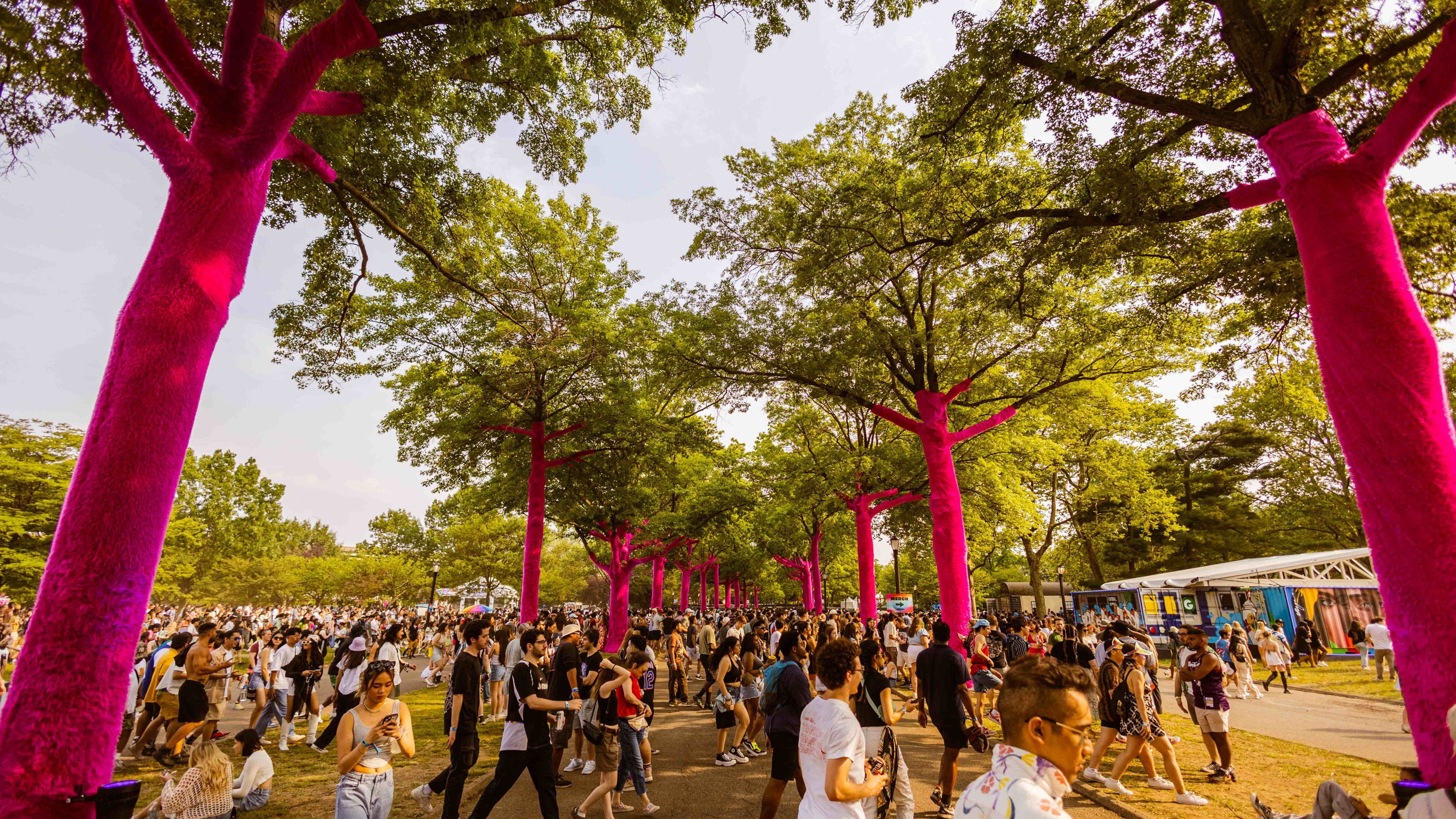 Founders Entertainment The Governors Ball crowd walking across a pathway flanked by trees wrapped in bright soft magenta fake fur