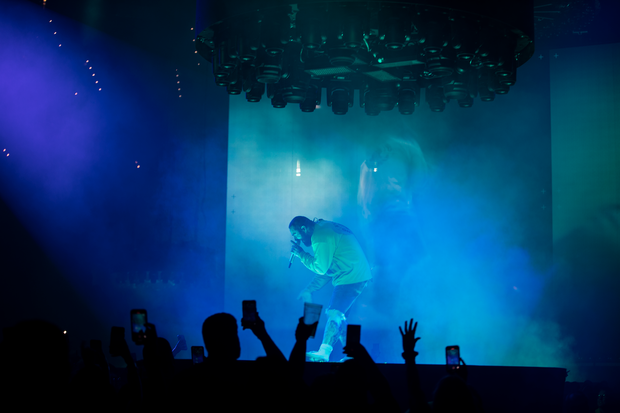 Post Malone bent over singing on stage with blue lighting