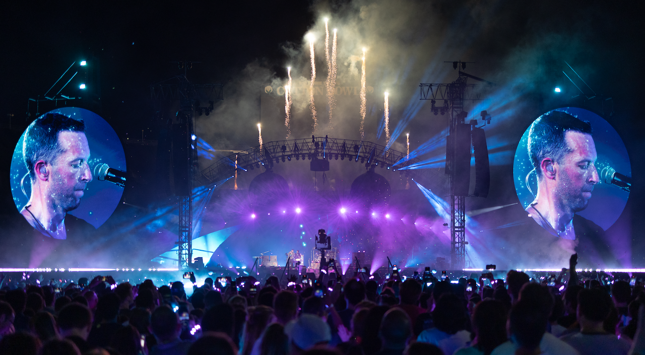 Chris Martin on LED screens singing to crowd with blue and purple lights