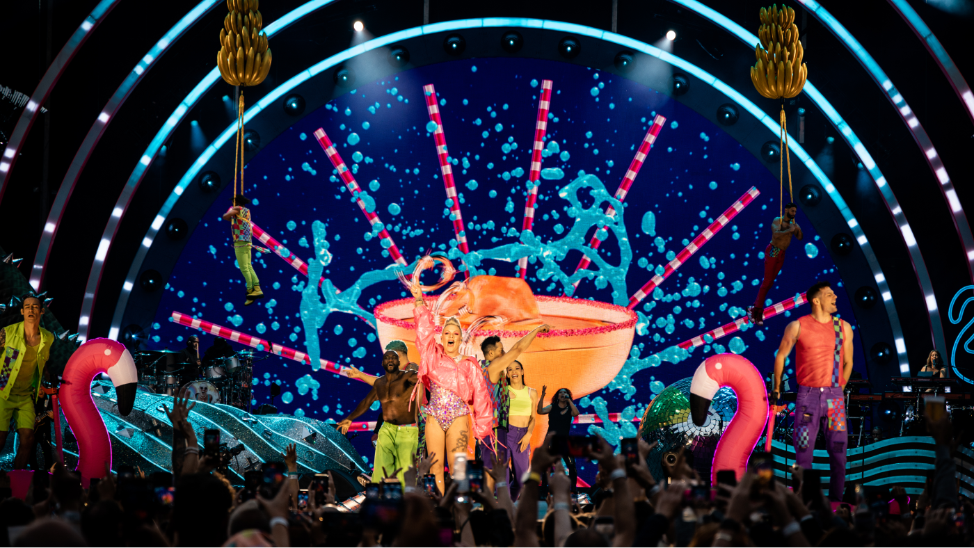 close up of p!nk performing on carnival-designed stage with her backup dancers