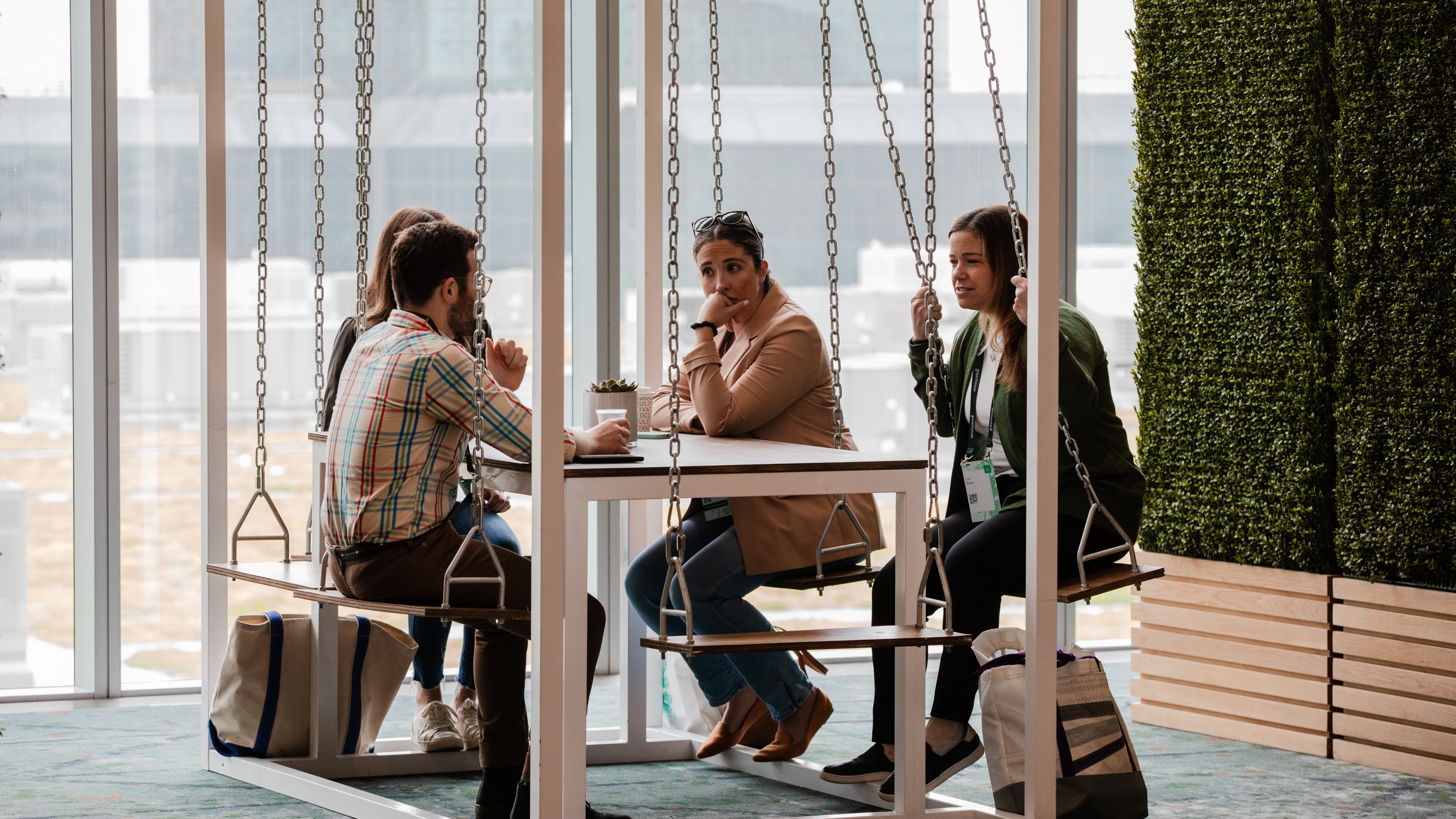 group of people sat at a table next to green wall and window looking onto city
