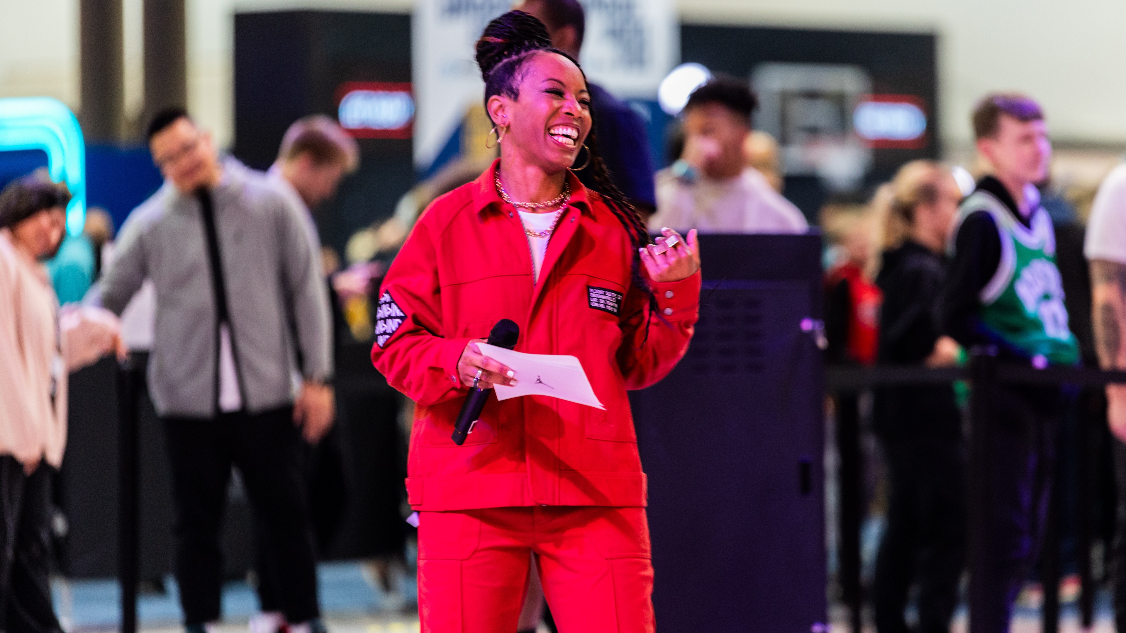 Woman wearing red jacket and trousers smiling holding sheet of paper and microphone