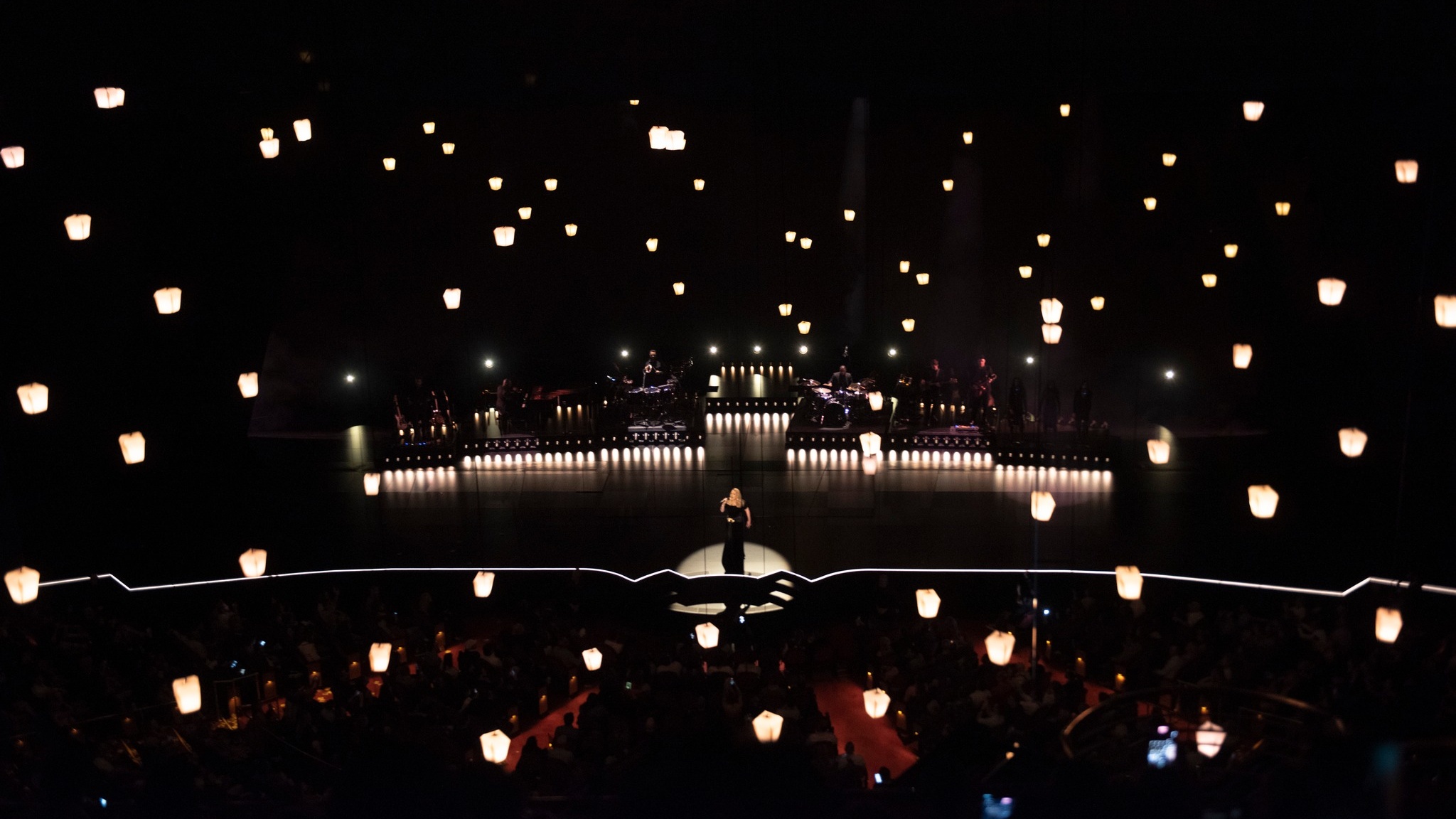 Singer Adele performing on stage under spotlight with lanterns floating around the venue