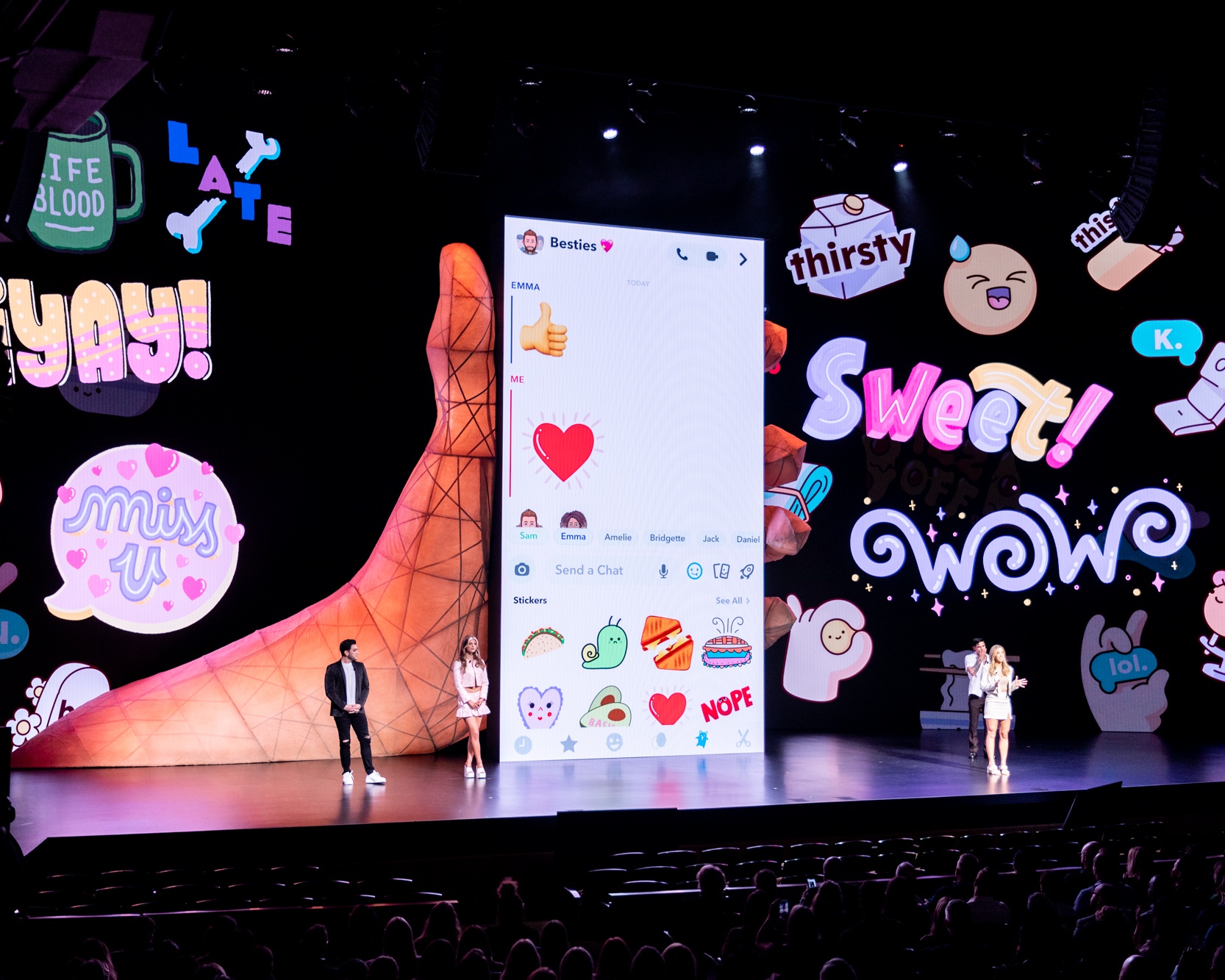 People on stage in front of a giant hand holding a cell phone