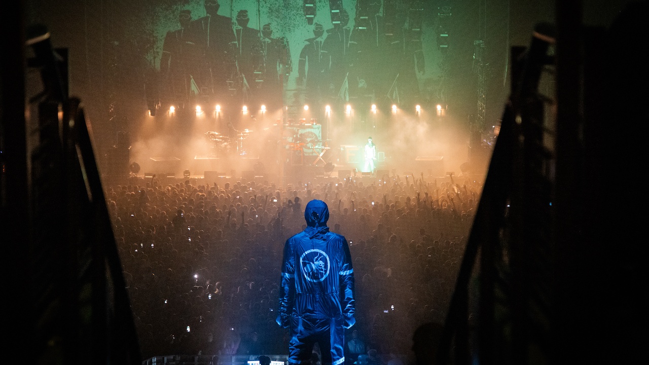 Huge sculpture of man in overalls with logo printed on the back overlooking huge crowd cheering the band on stage