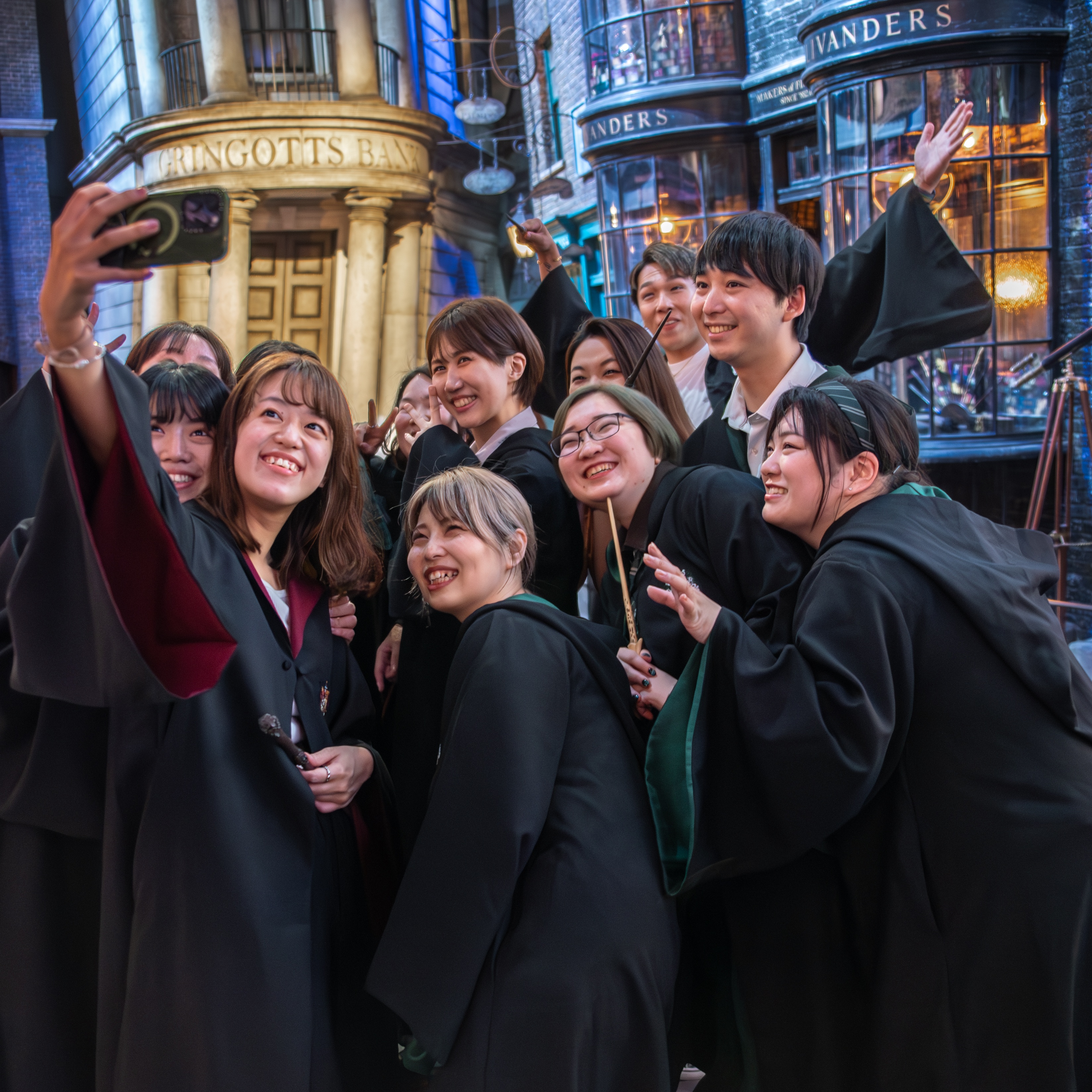 A group of Harry Potter fans in robes taking a selfie in front of Diagon Alley