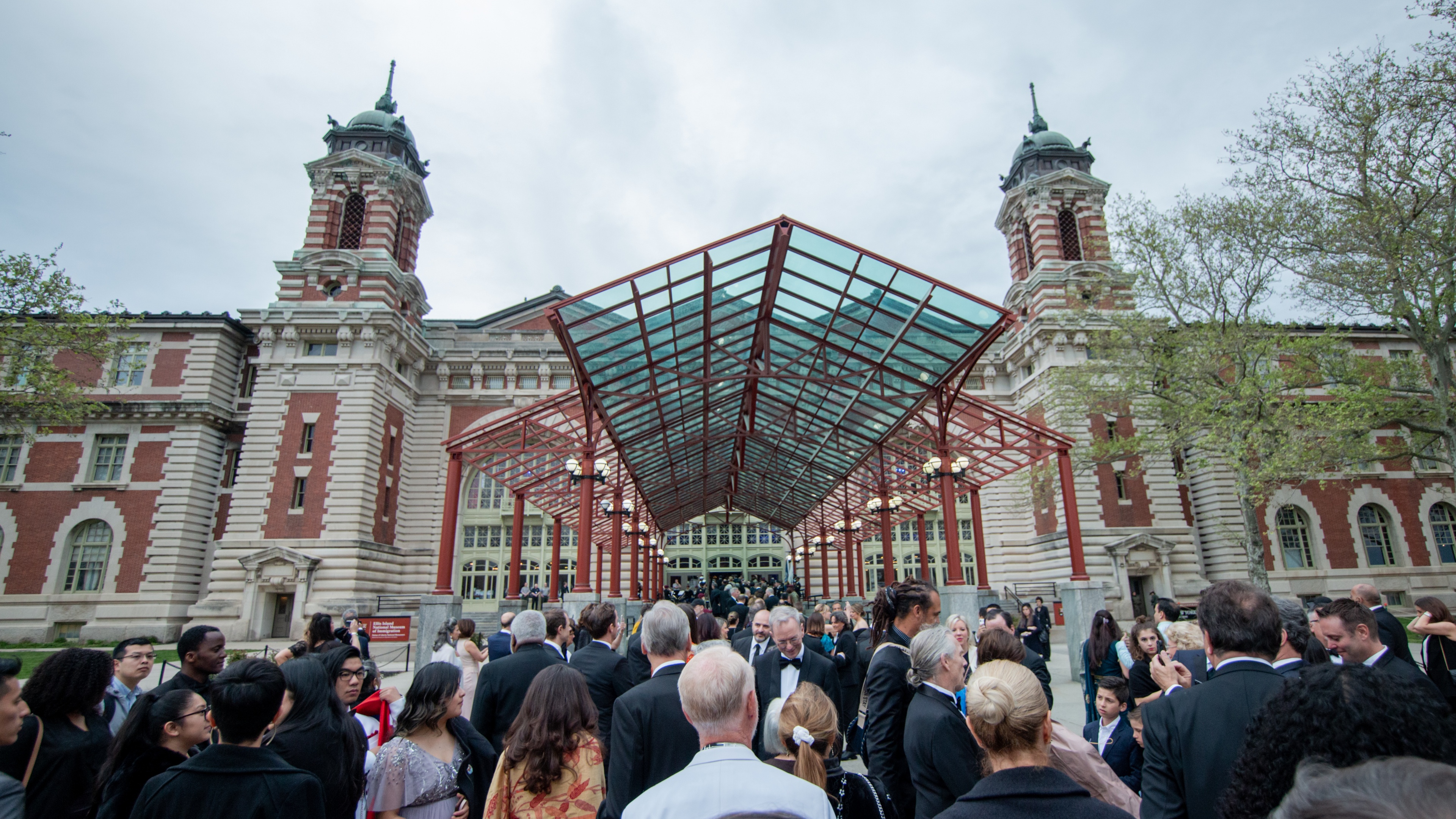 crowd of people gathered outside grand looking brick building with glass roof entrance