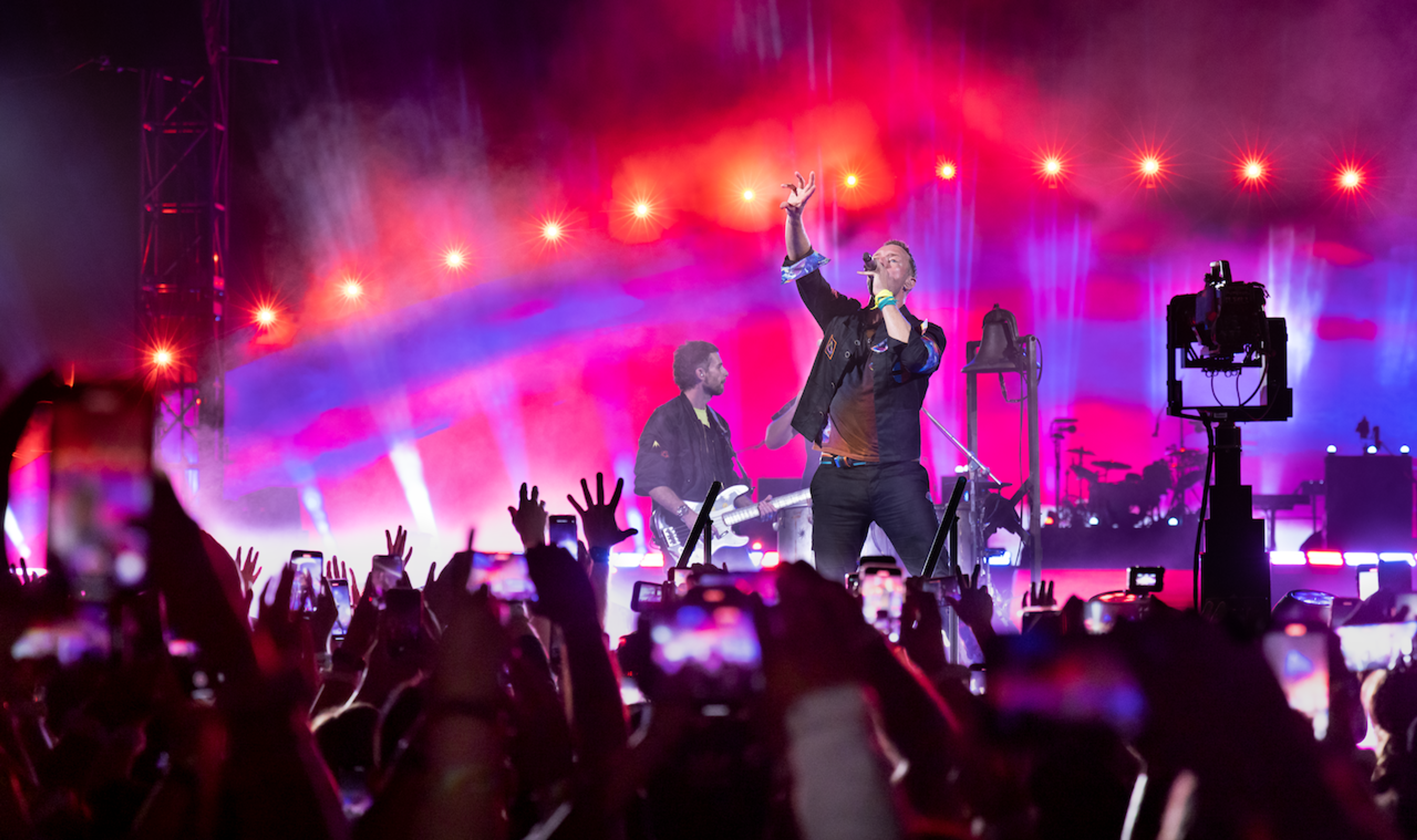 Coldplay performing in front of cheering crowd with pink and purple stage lights