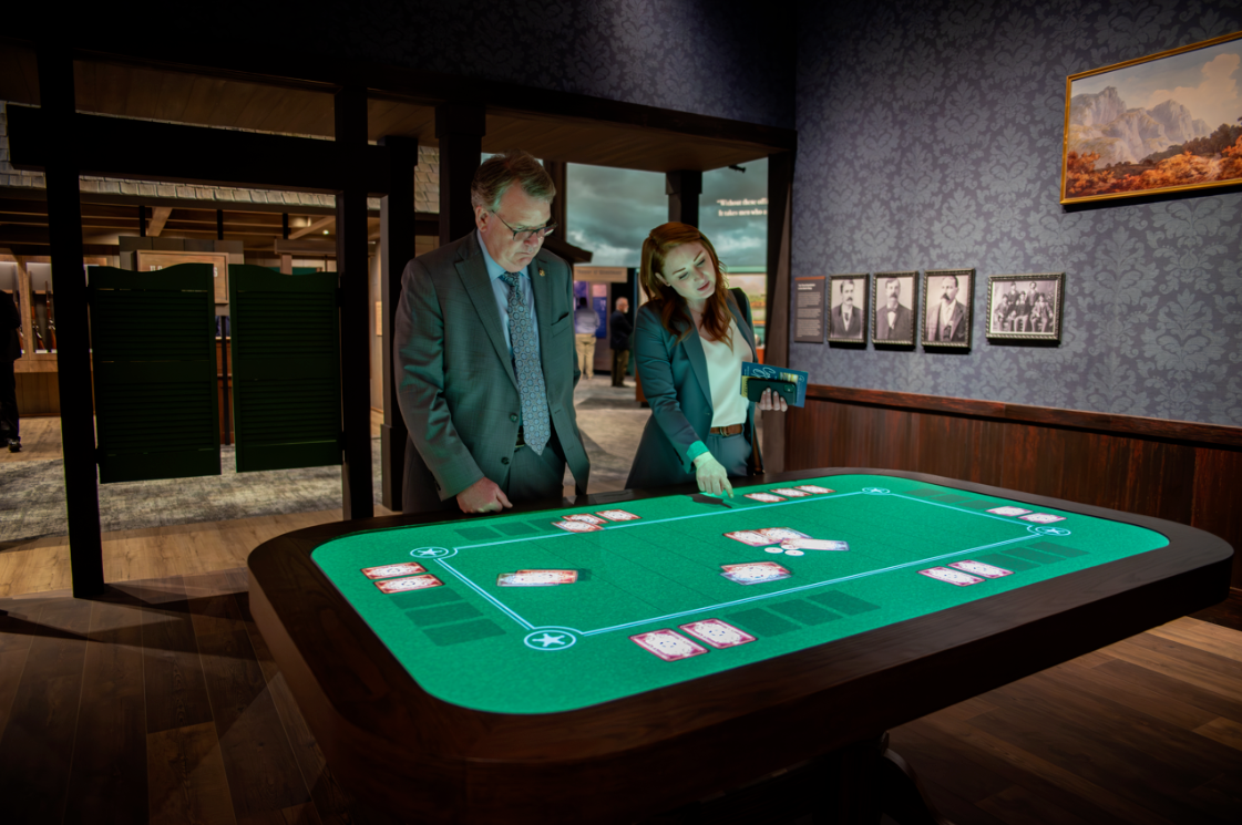 Two museum-goers interacting with a digital green table with cards displayed on it in a game format