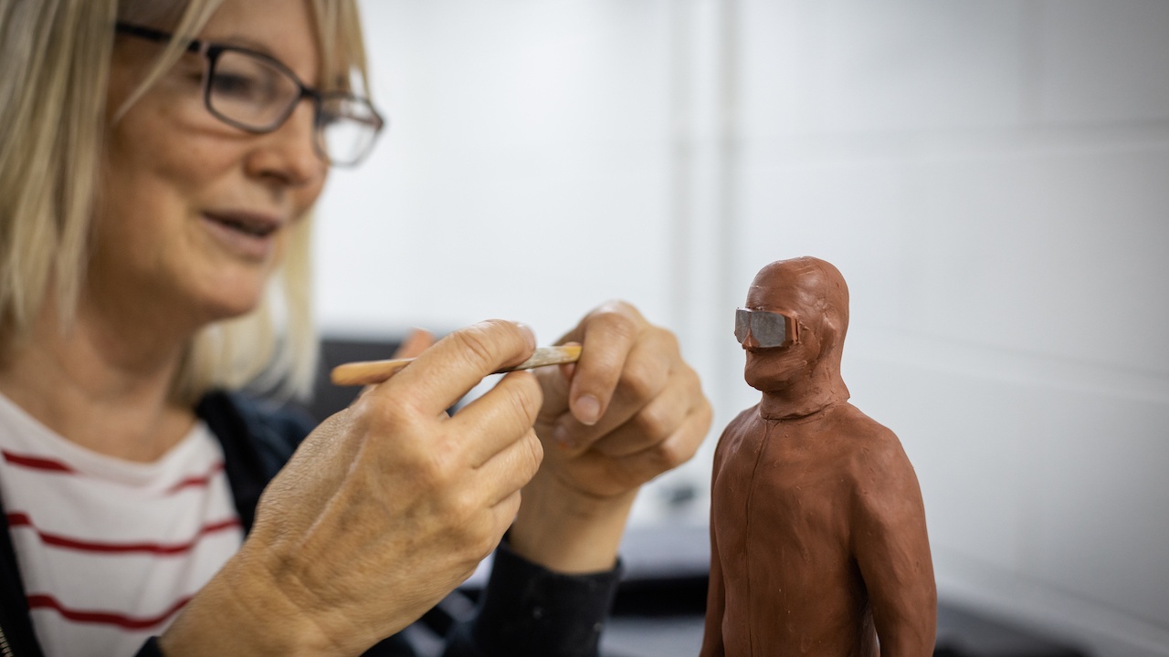 Woman intricately working on 3D model of man made out of clay