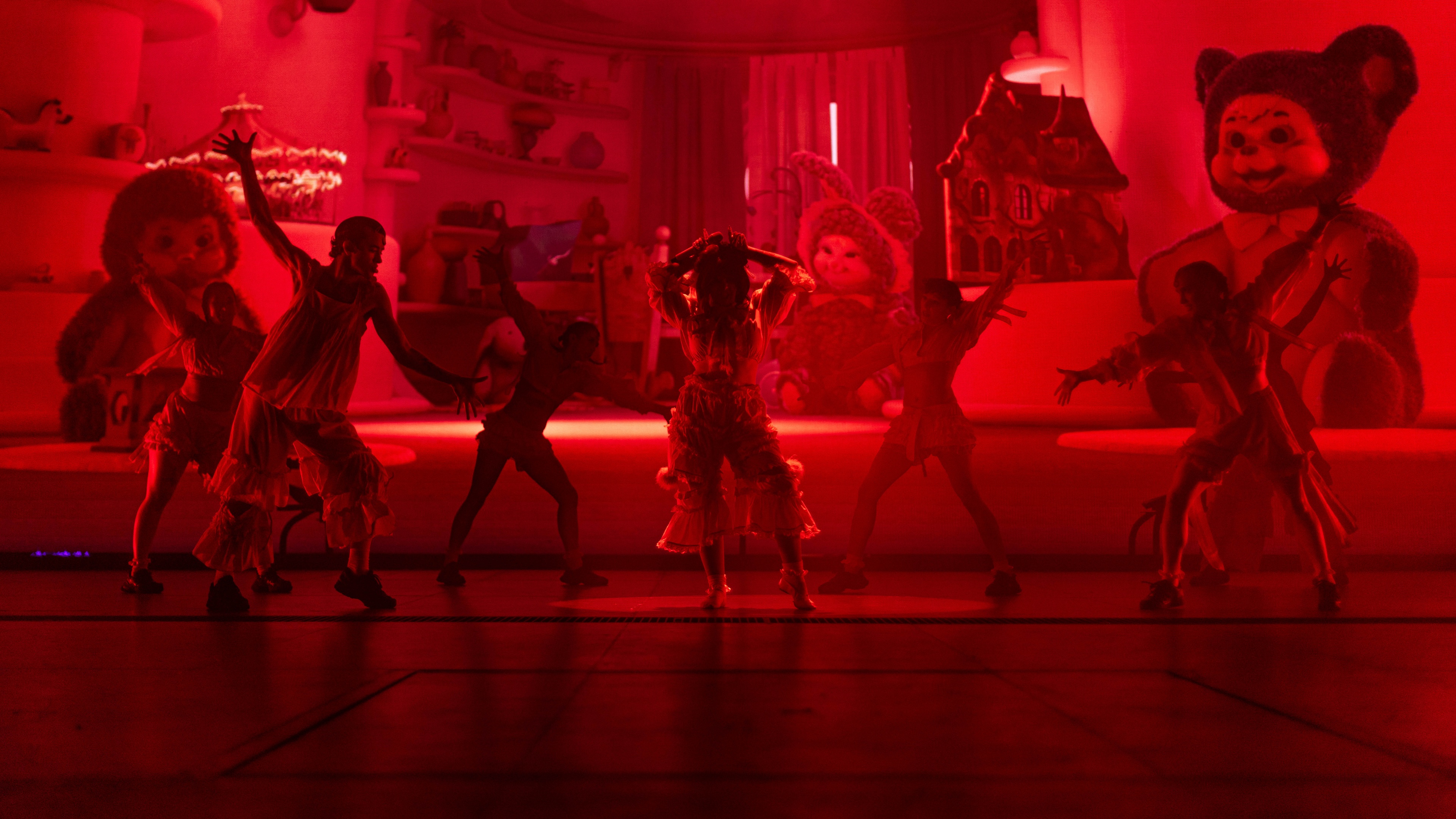 Performers on stage with large kid toys in the back and red lights