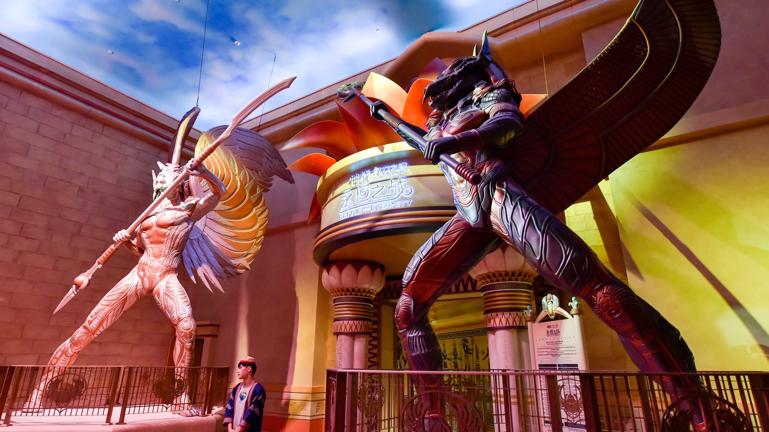 Giant sculptures guarding entrance to theme park entrance with person stood underneath