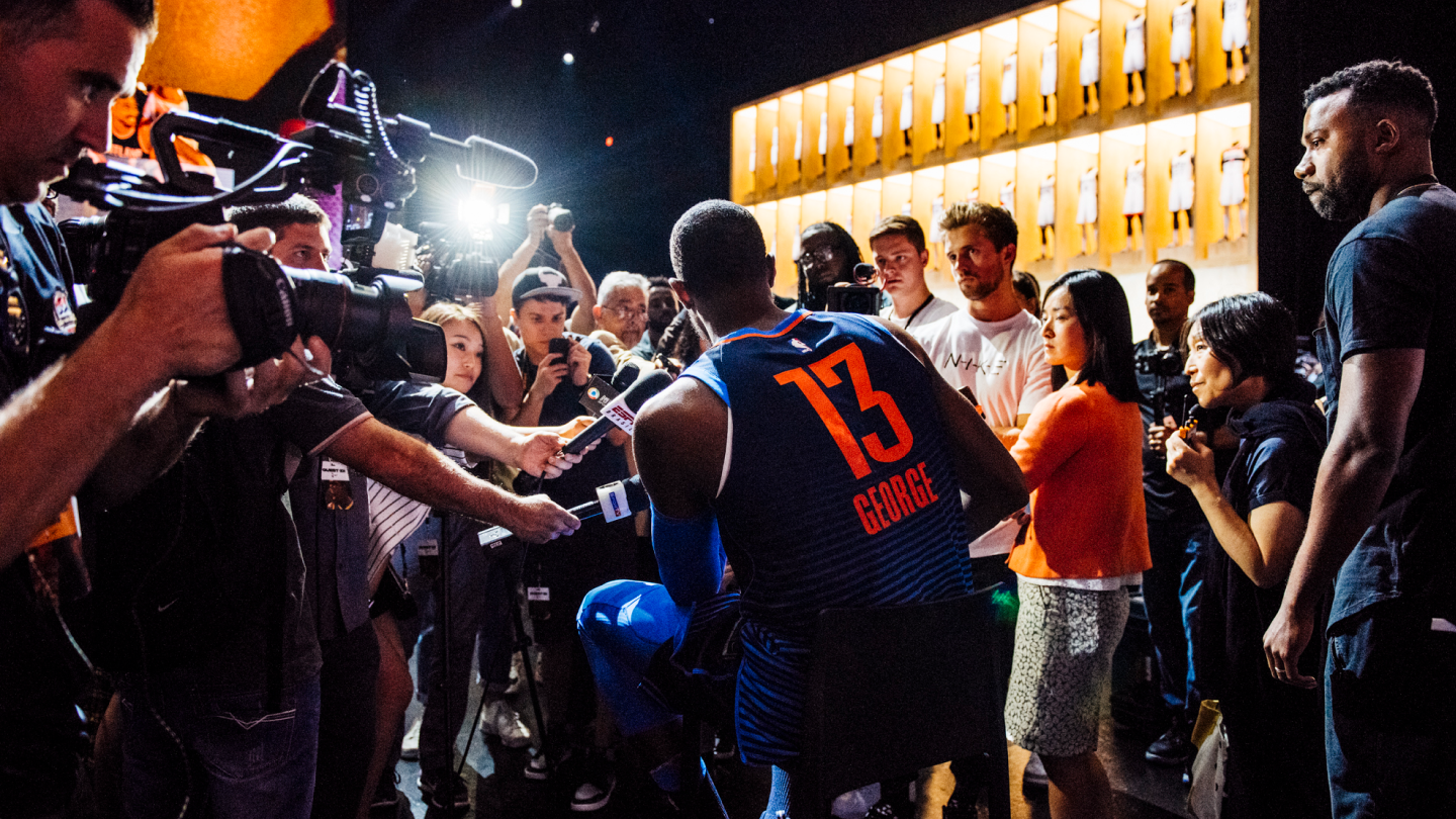 basketball player surrounded by press with cameras and microphones interviewing him