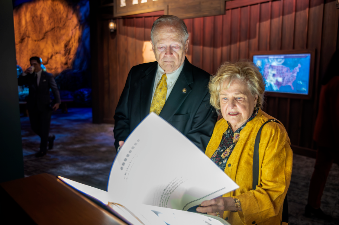Two museum-goers flipping a large book page with interactive historic material on it