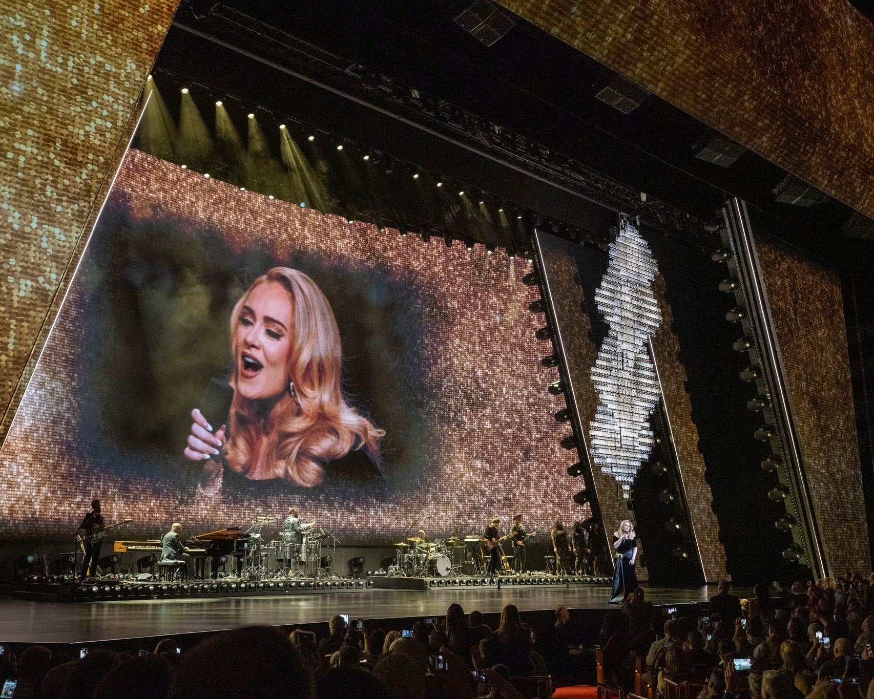 Singer Adele performing on large stage with band in front of Gold shimmer staging and live video of her on a huge LED screen