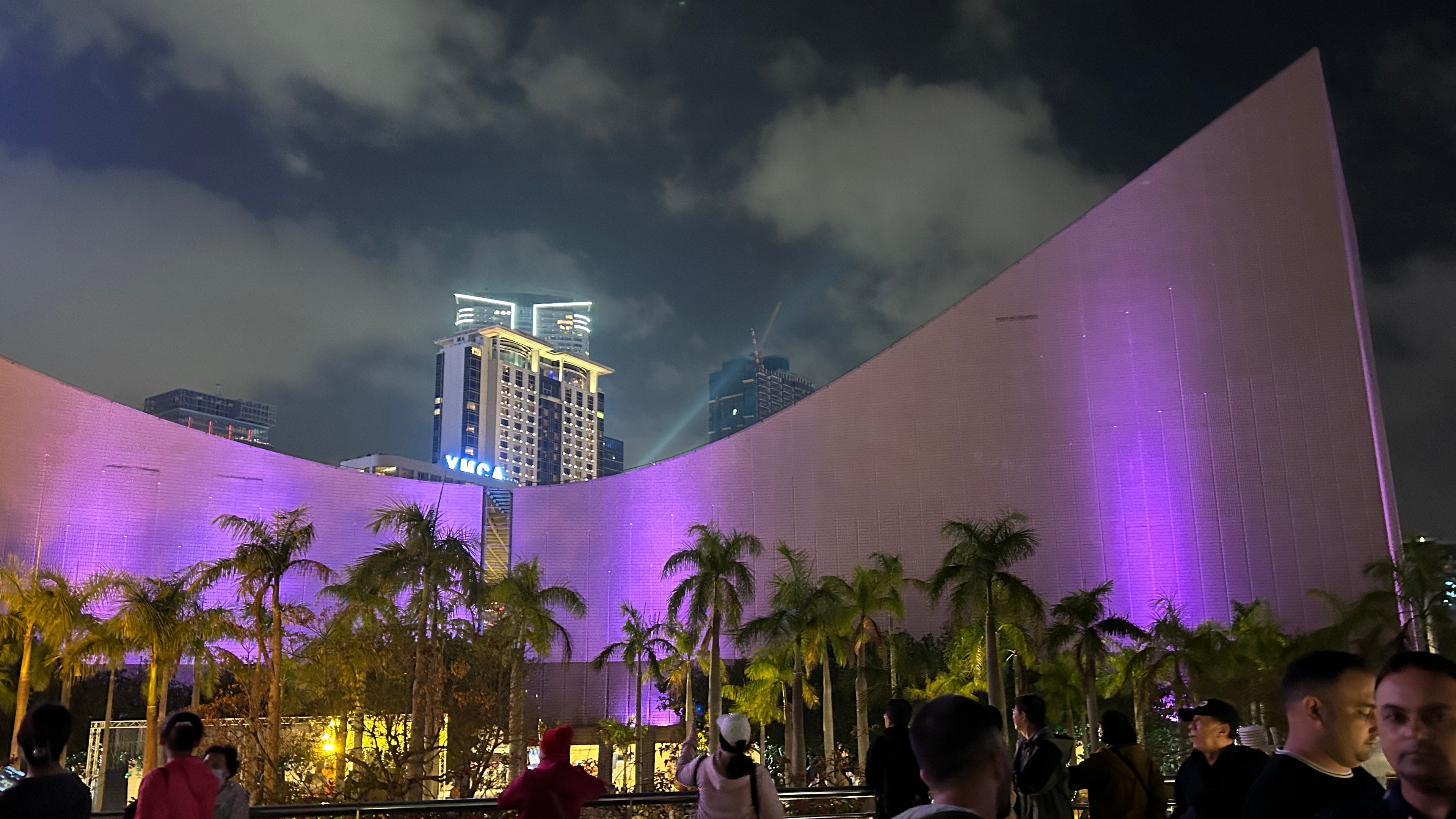 Hong Kong Cultural Center a night with purple spot lights large group of people and palm trees
