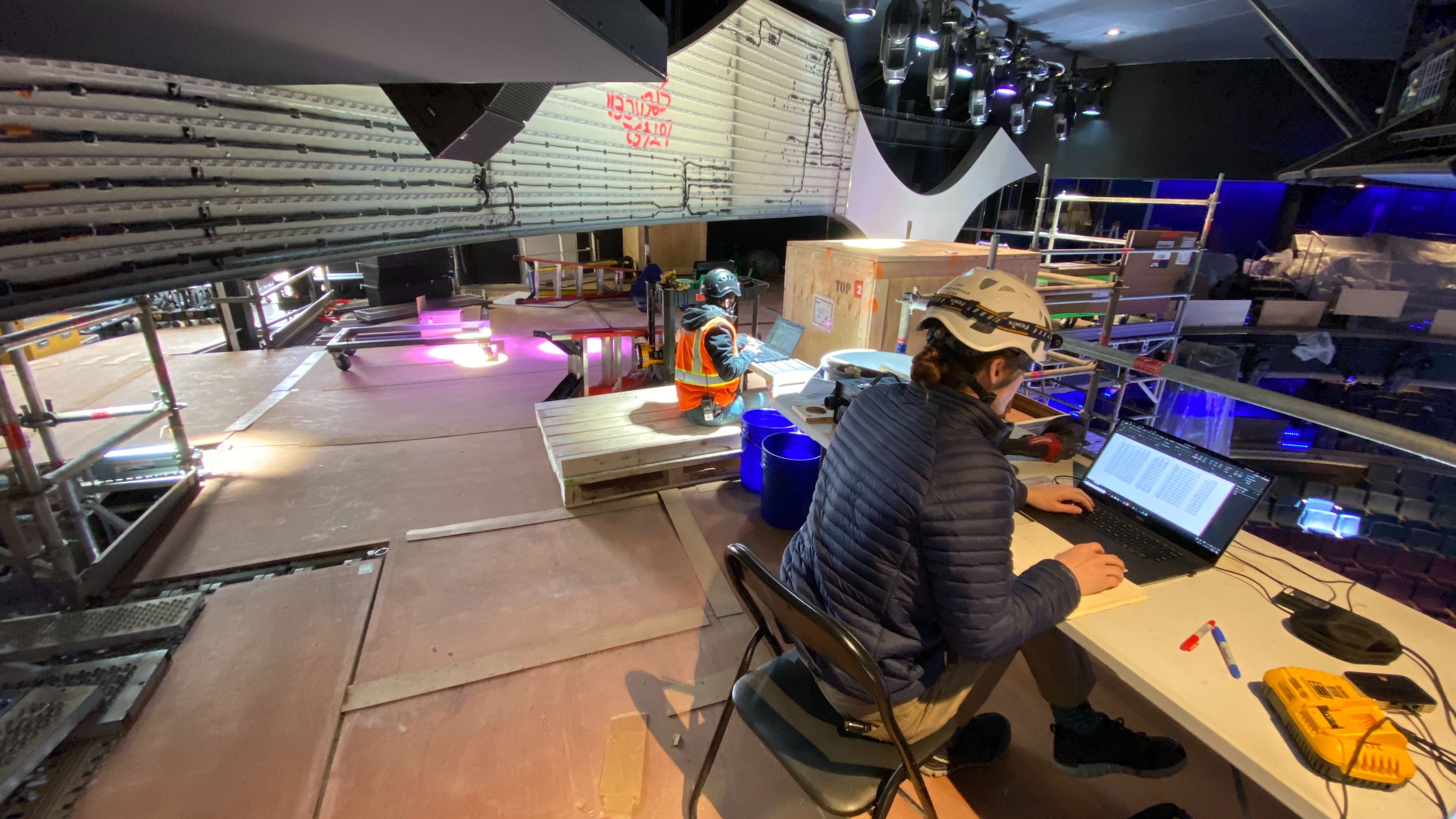 Woman operating laptop and worker in hi vi looking down at seating arrangement