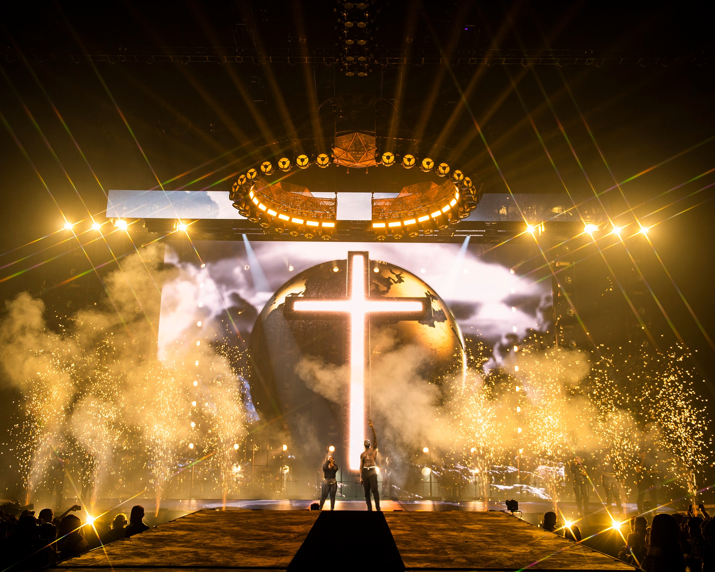 Rapper Stormxy performing on stage with gold chandelier gold lighting in front of a cross and globe with pyro effects