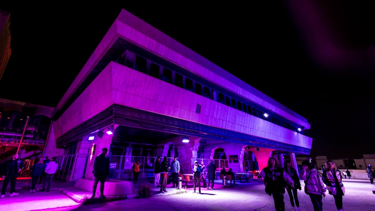 People gathering round industrial building under purple lighting