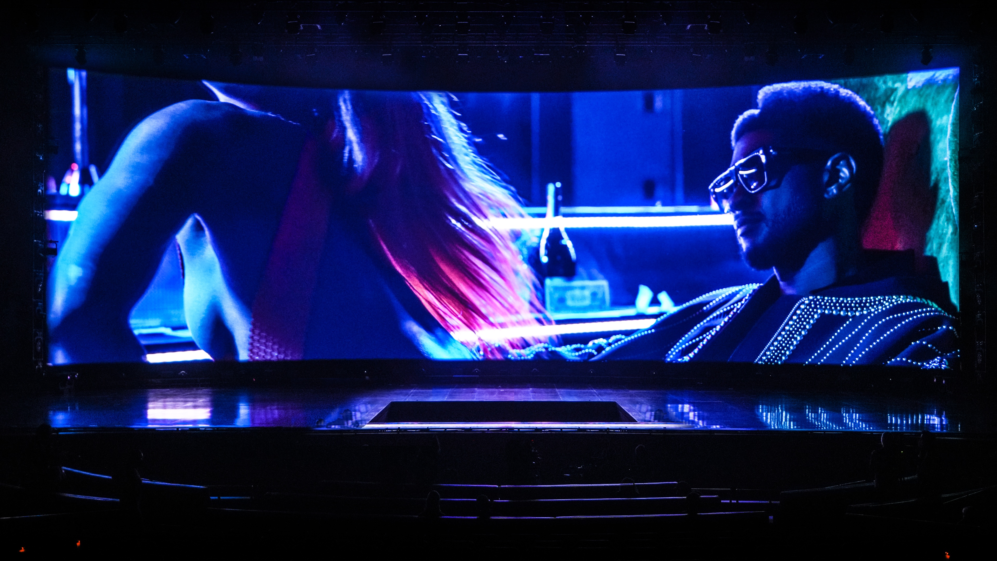 Usher Residency at The Colosseum at Caesars Palace empty stage featuring a super wide screen featuring a close up of user wearing sunglasses sitting on a green chair checking out female sitting on his lap