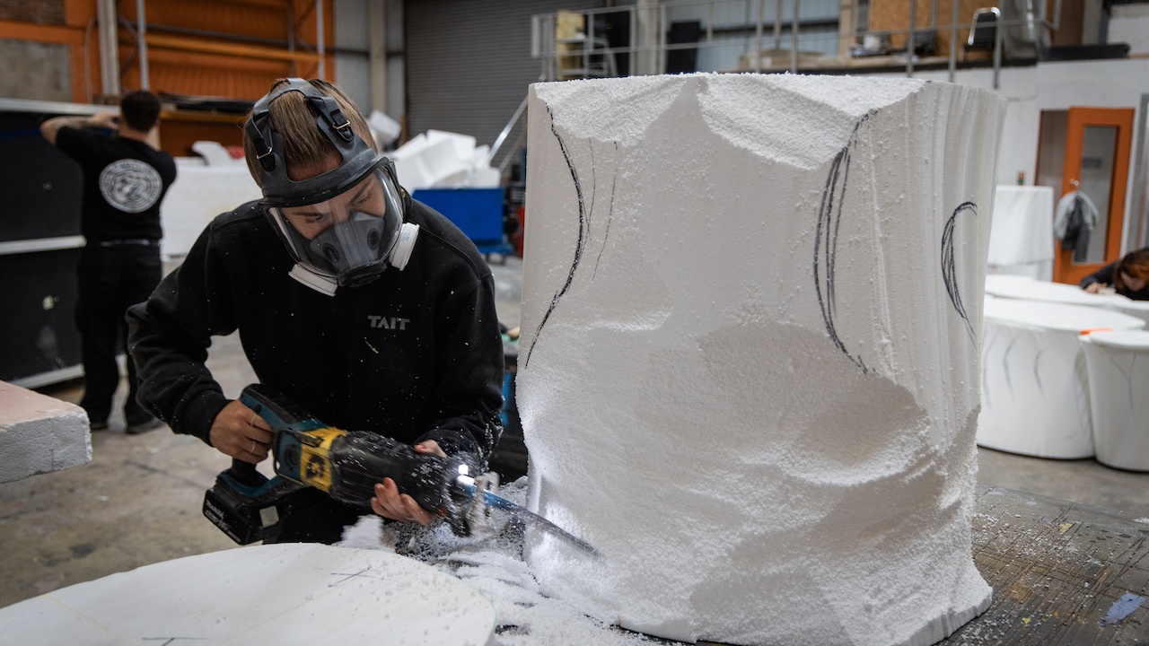 Woman wearing face mask sawing away polystyrene to reveal sculpture