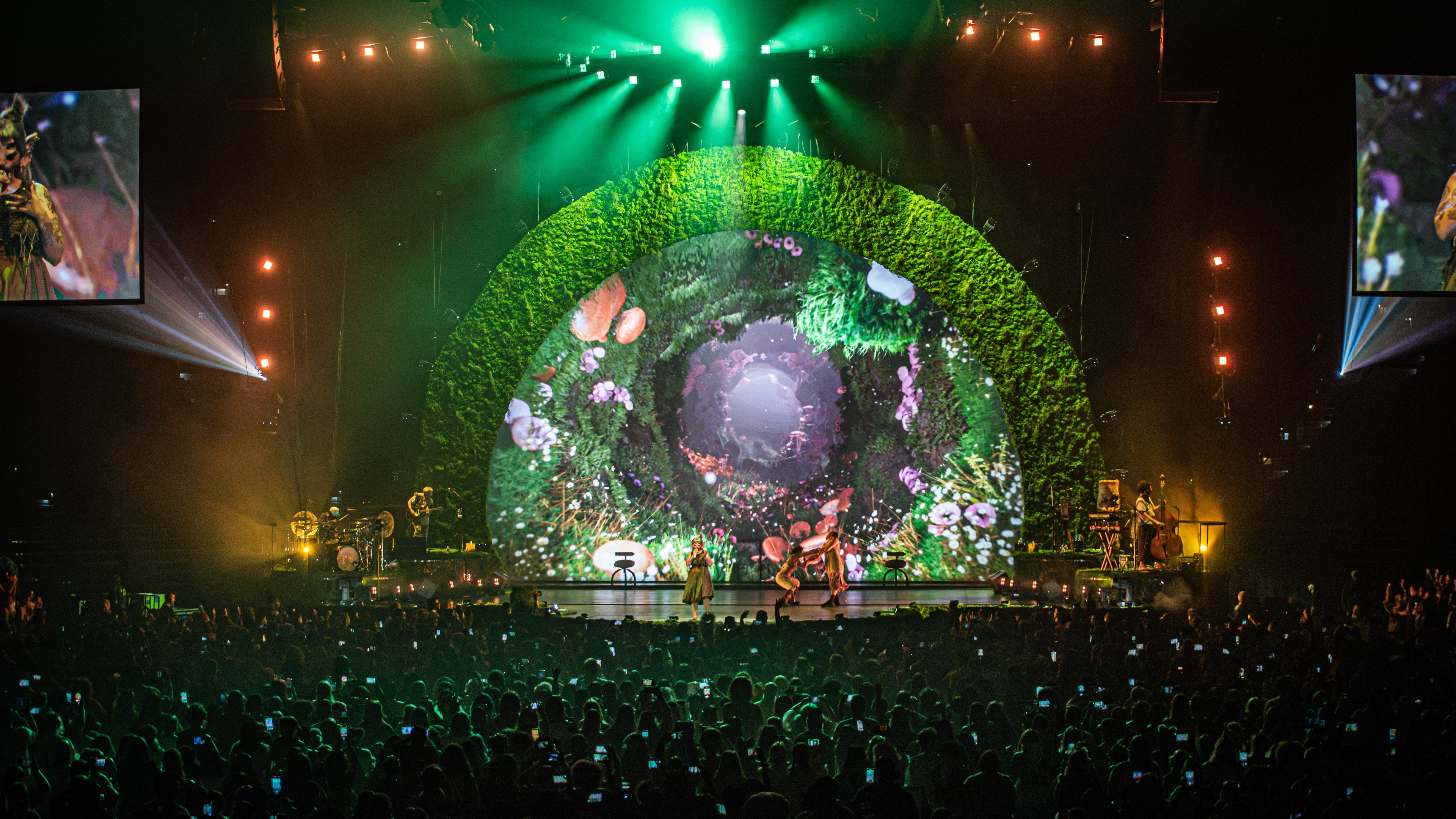 Stage with green plant arch with green lighting and large crowd