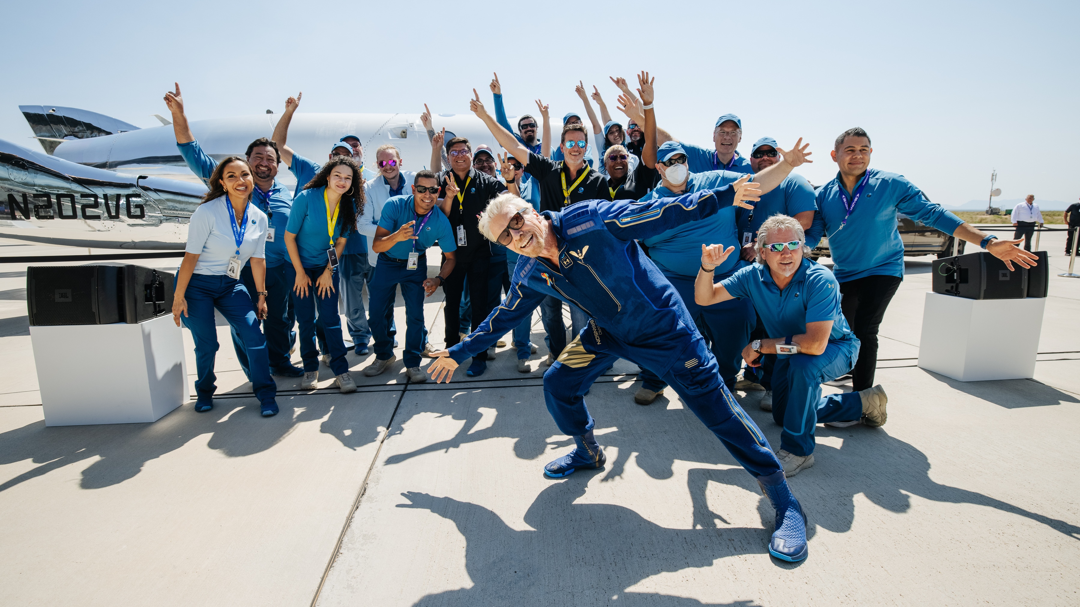 Richard Branson posing in front of a group of people all dressed in blue