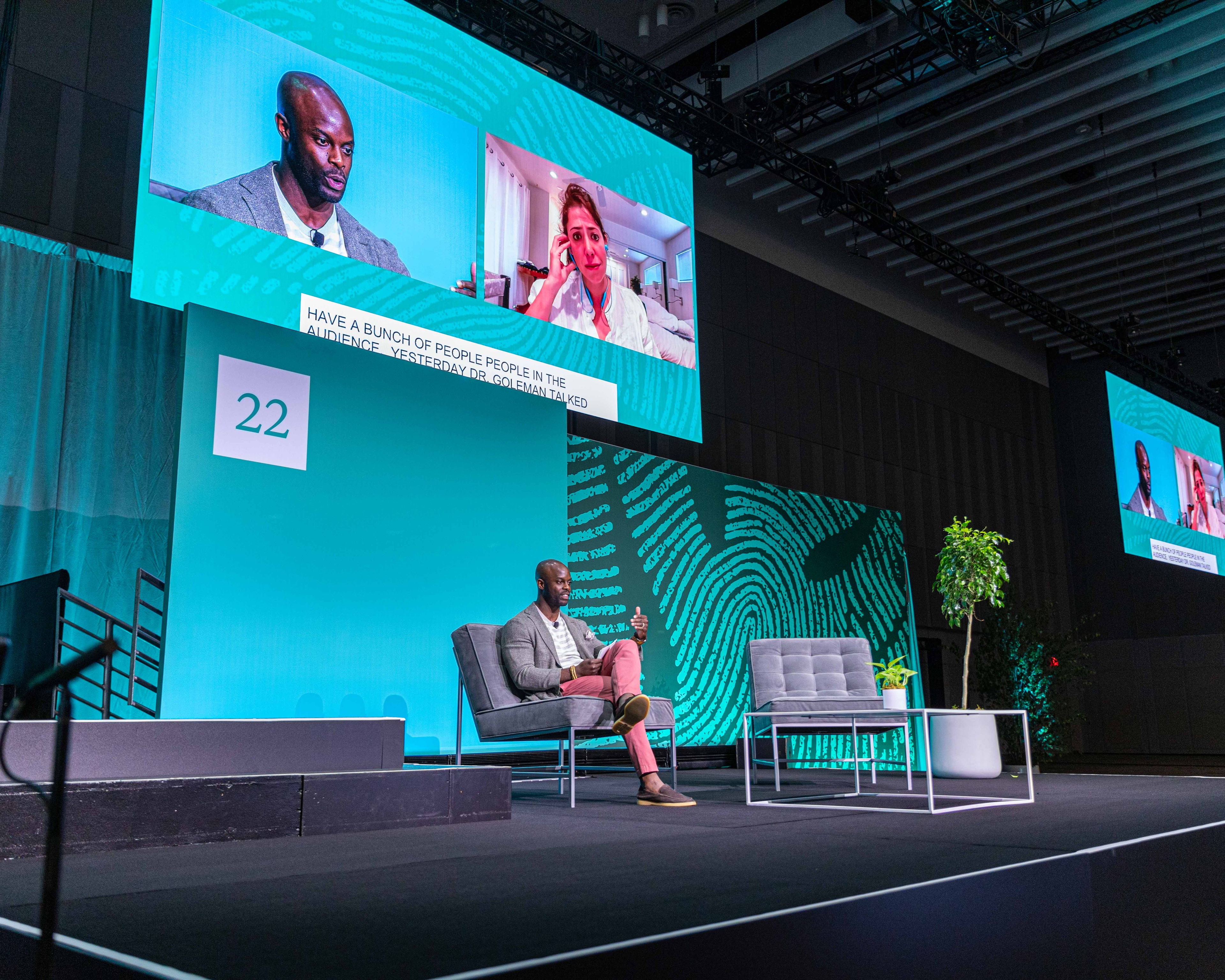 person sat on stage giving a talk in front of blue backdrop at Greenhouse conference 2022