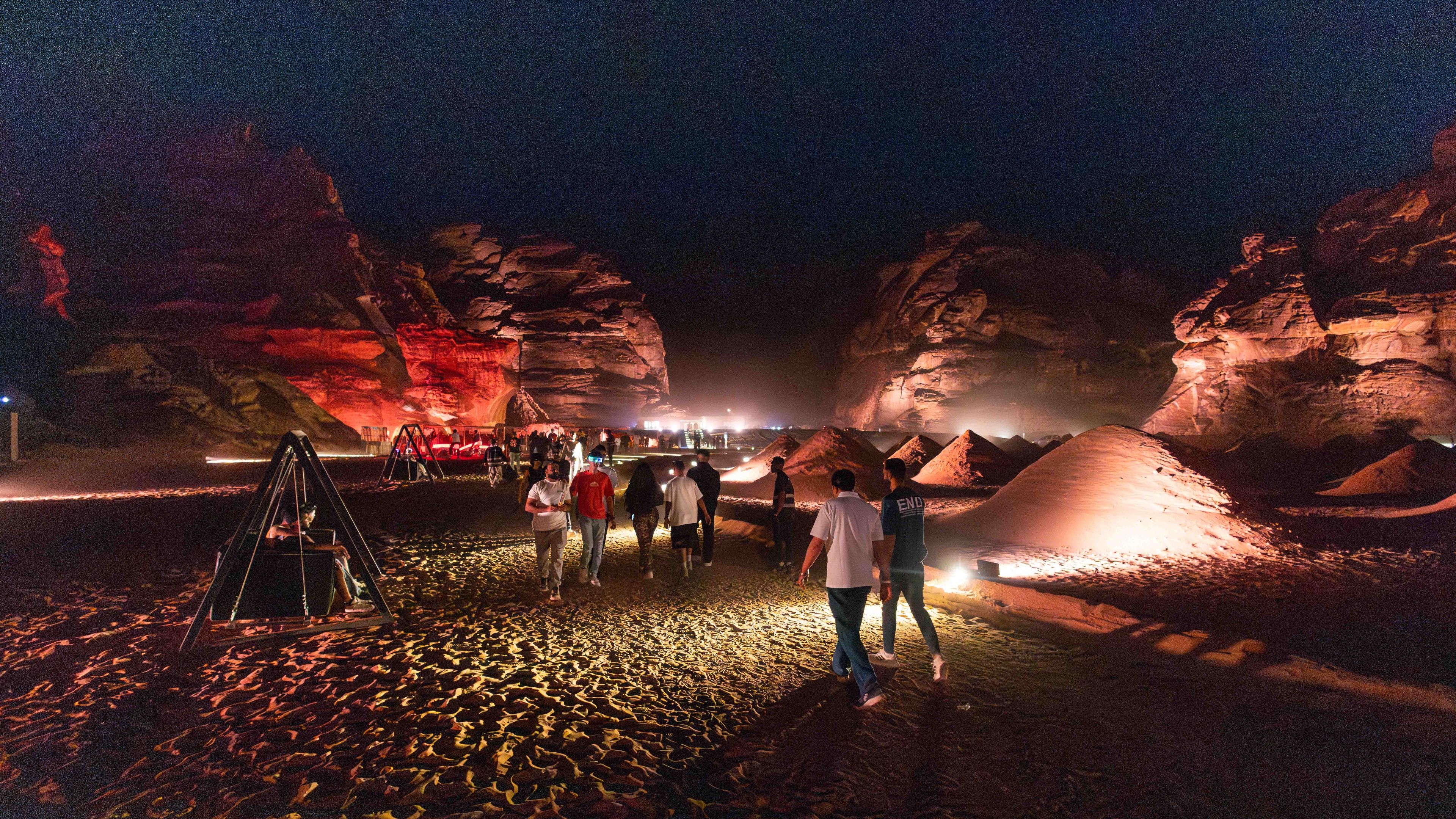 People entering festival site in the middle of the desert between rocky landscape on sand with red lighting