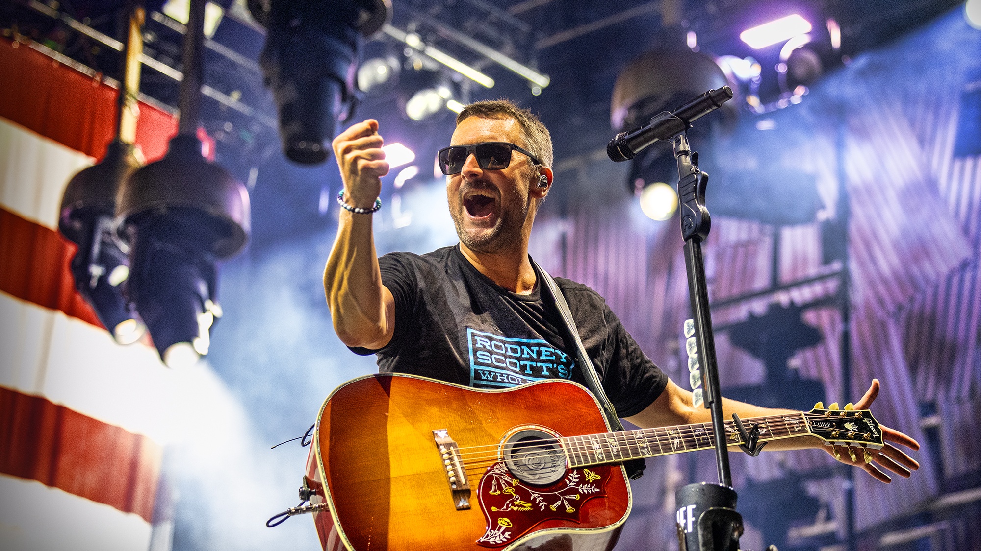 Country singer Eric Chruch interacting with the crowd holding guitar with American flag in the background