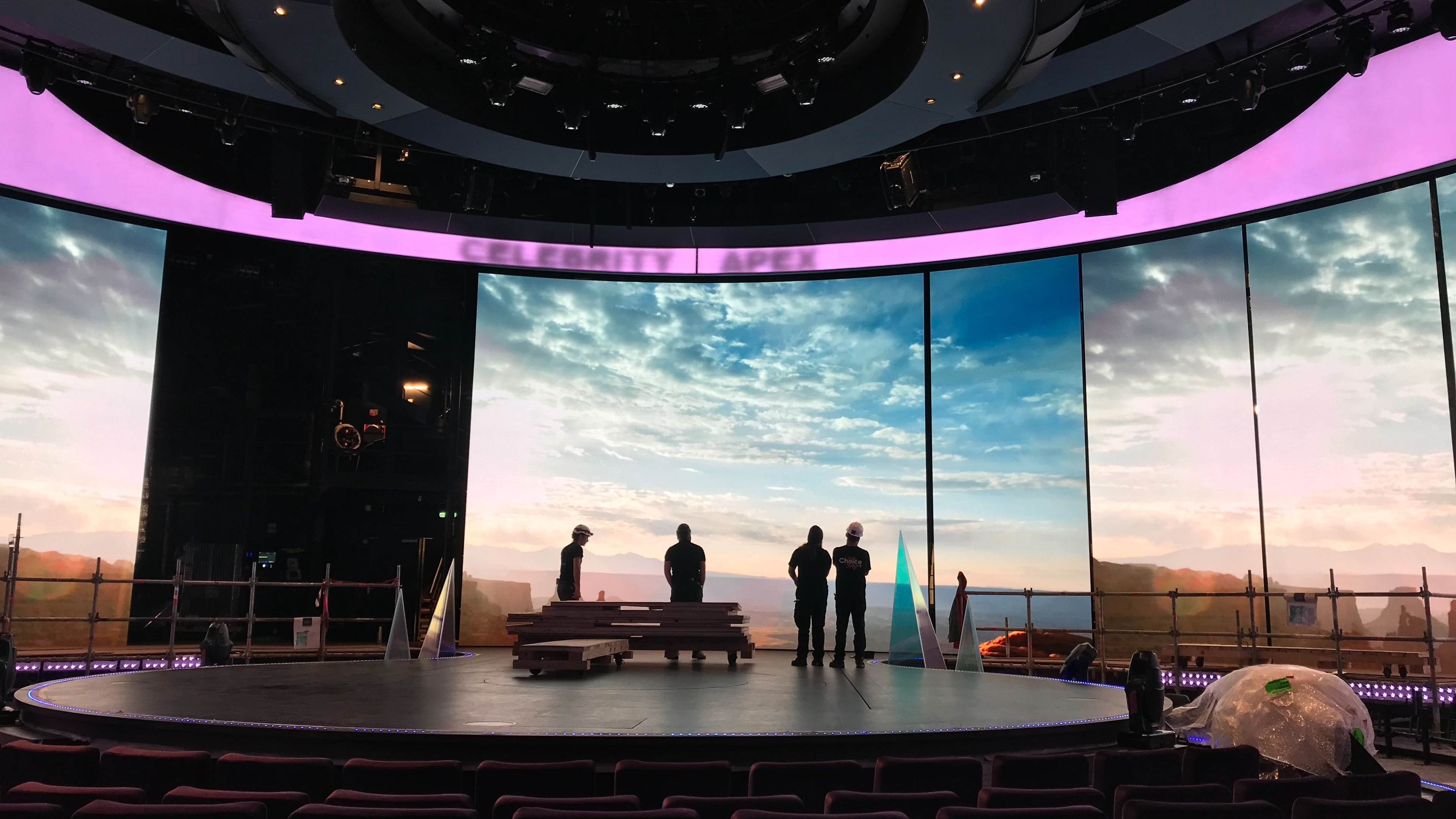 Group of workers stood on stage looking at huge curved LED screen mid construction