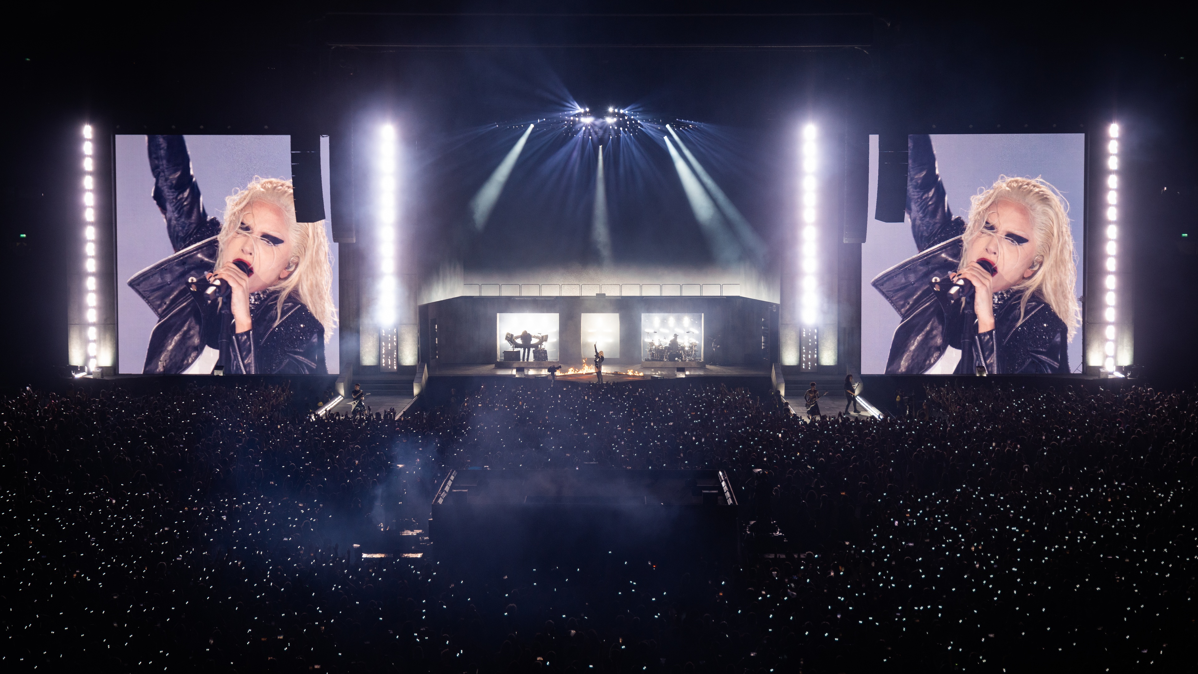 Singer Lady Gaga performing on wide stage with white spotlights and videos of here on huge LED screens on the left and right