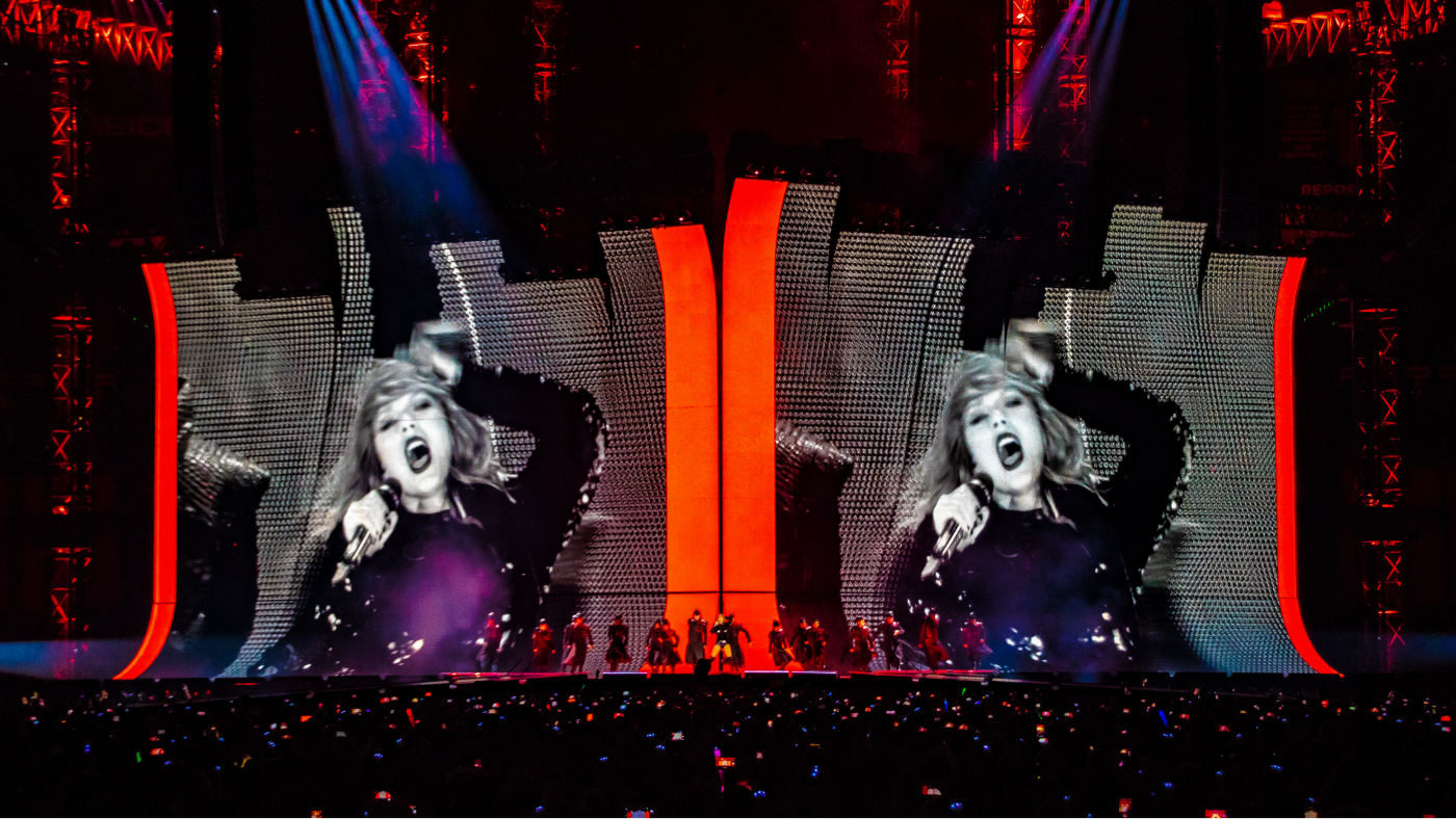 taylor swift performing on stage with her image projected on screen behind her