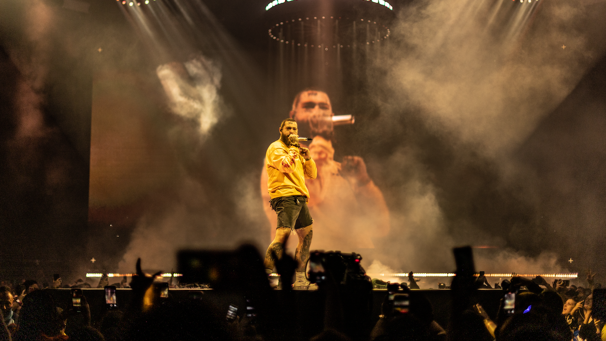 Post Malone on stage performing in yellow shirt with yellow stage lighting