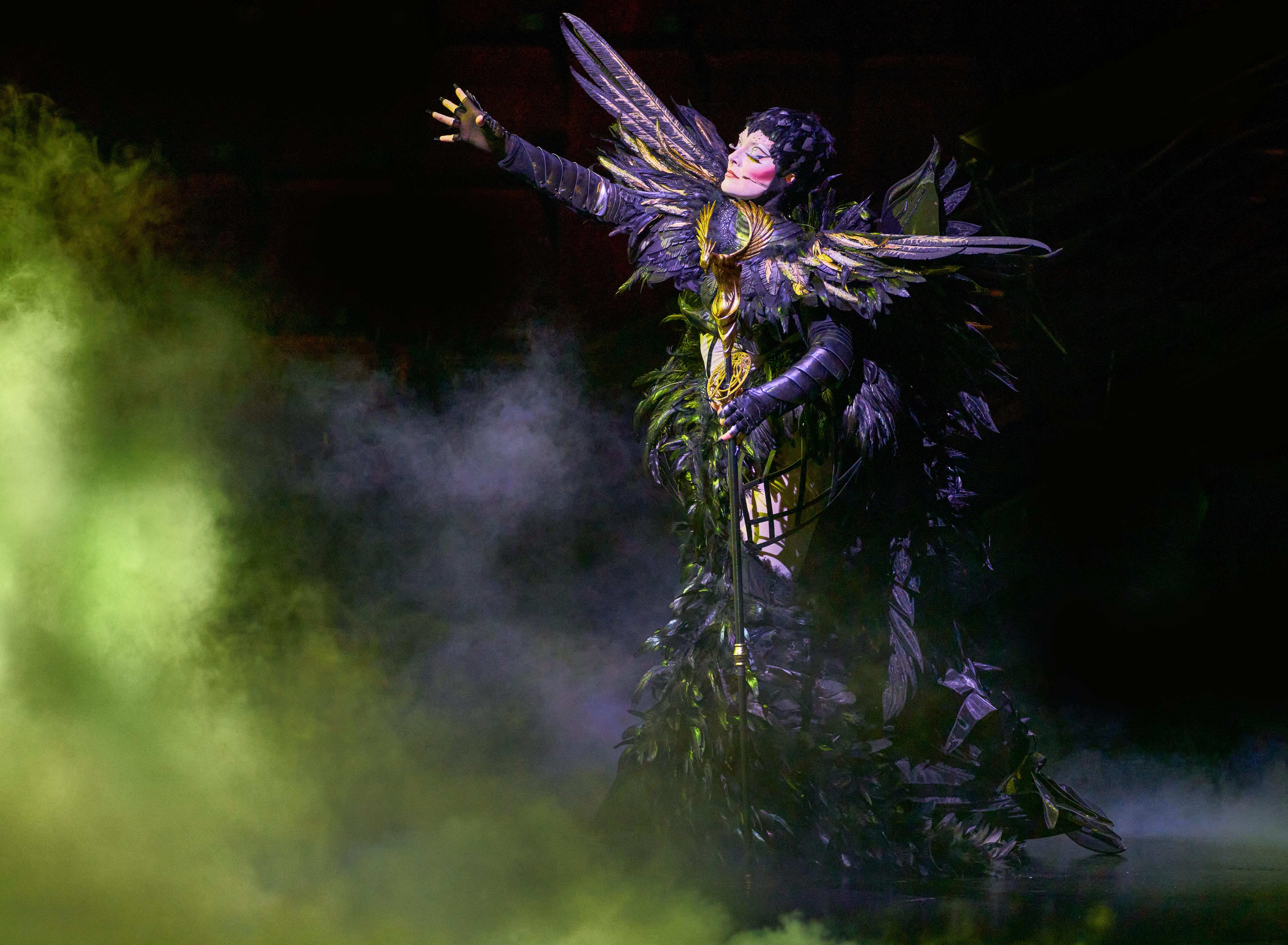 Awakening performer in black winged costume on stage with green fog