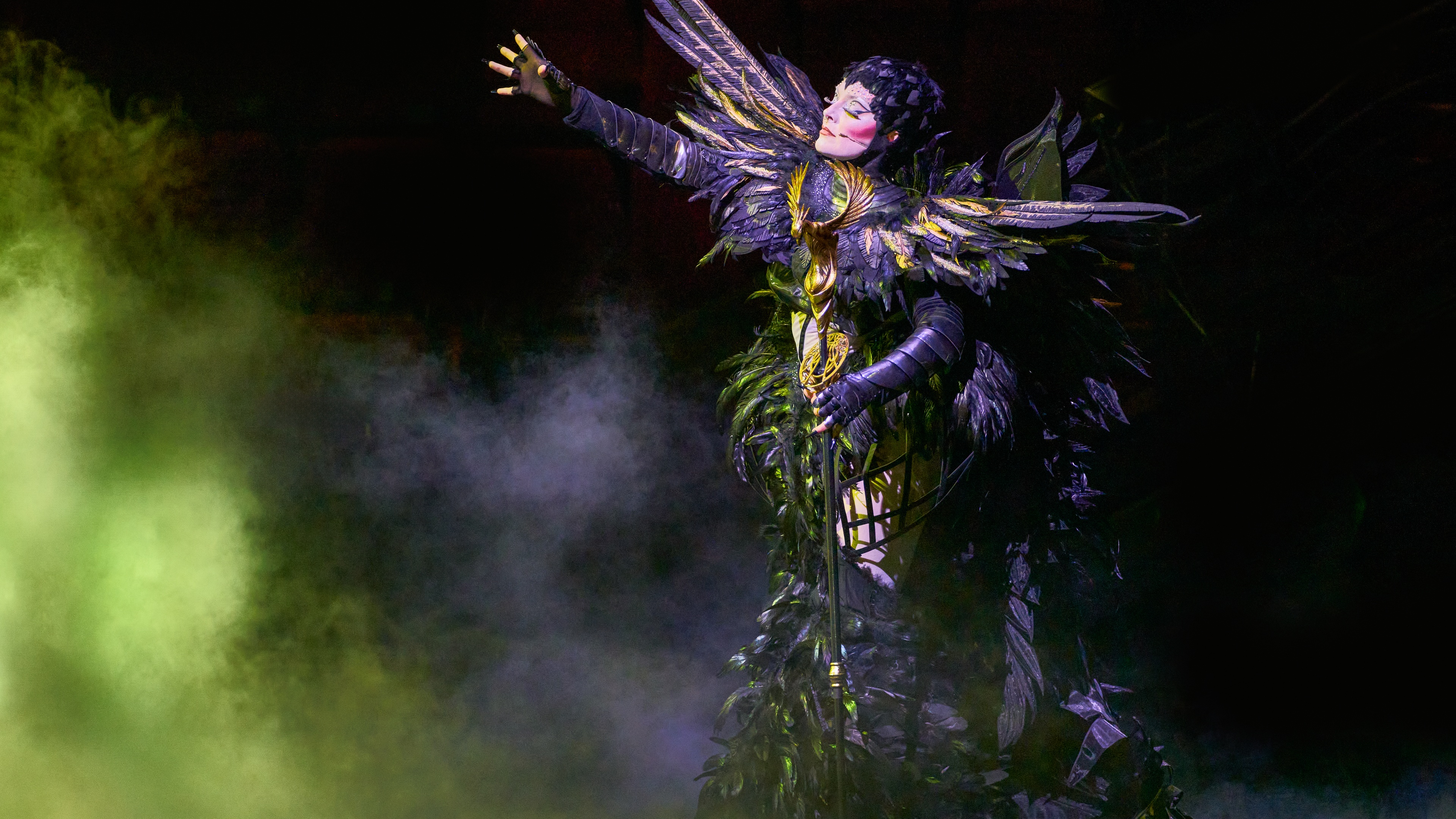 Awakening performer in black winged costume on stage with green fog