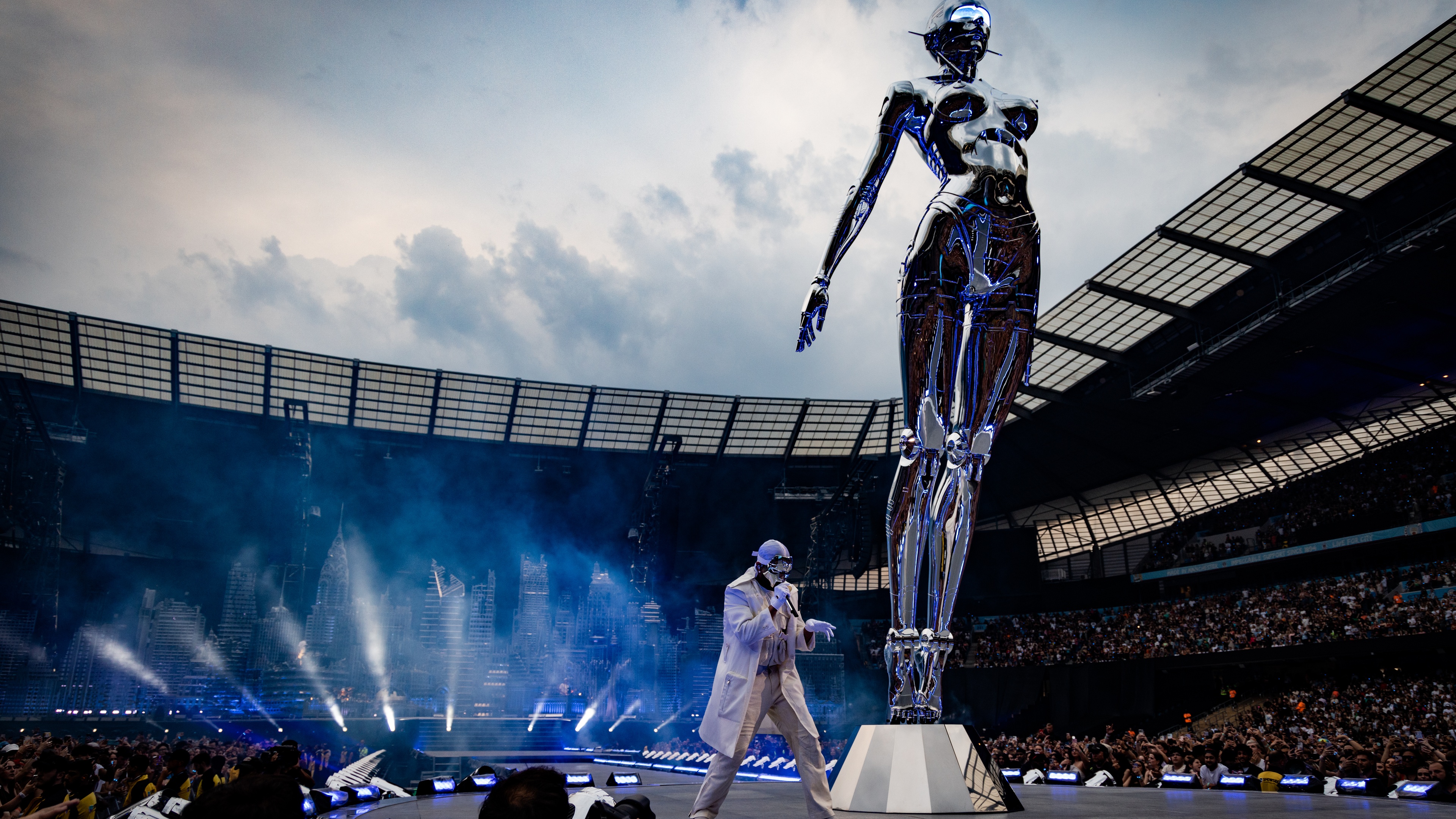 The Weeknd performing in the middle of stage inside stadium next to a huge robot sculpture
