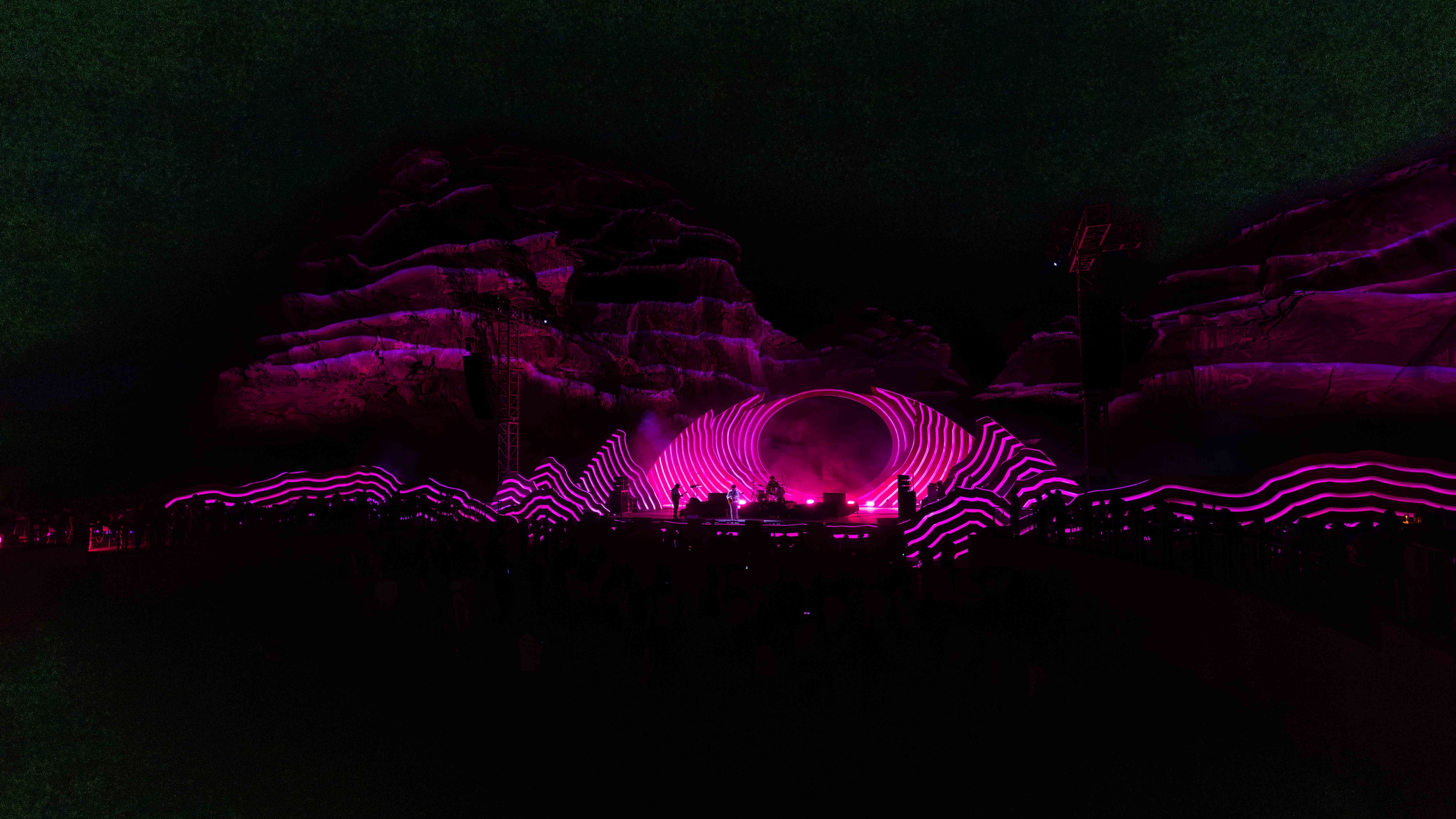 Night festival stage with pink lighting and rocky background