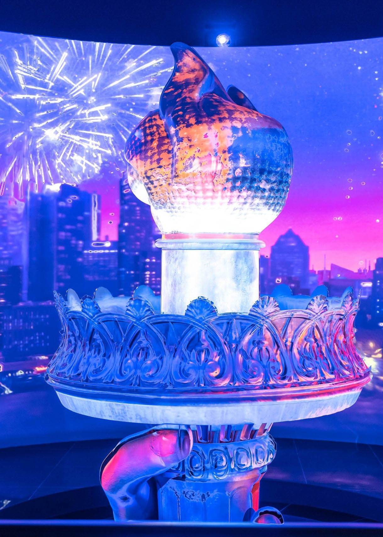 Statue of Liberty torch in front of LED screen showing fireworks over the New York City skyline