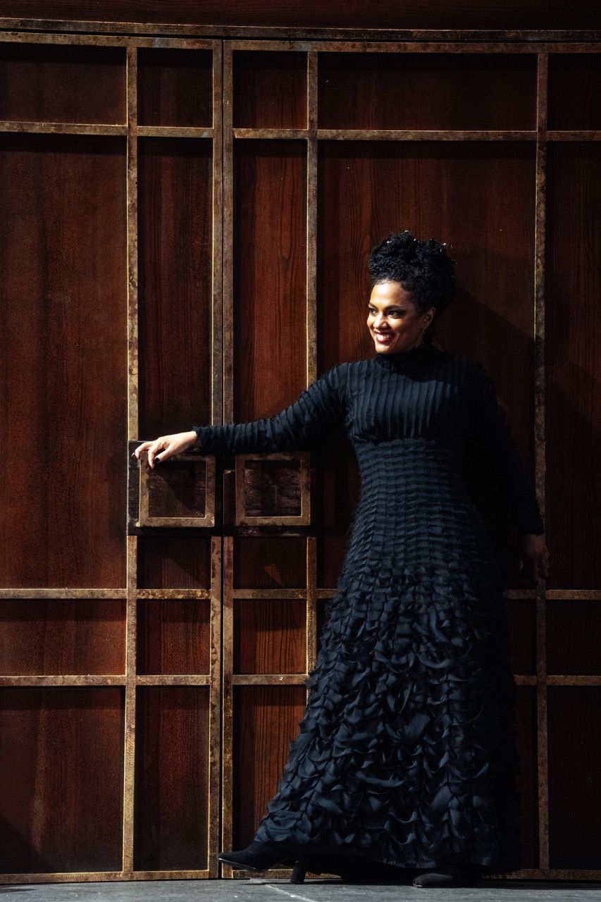 female performer in black dress posing in front of wooden decorated wall
