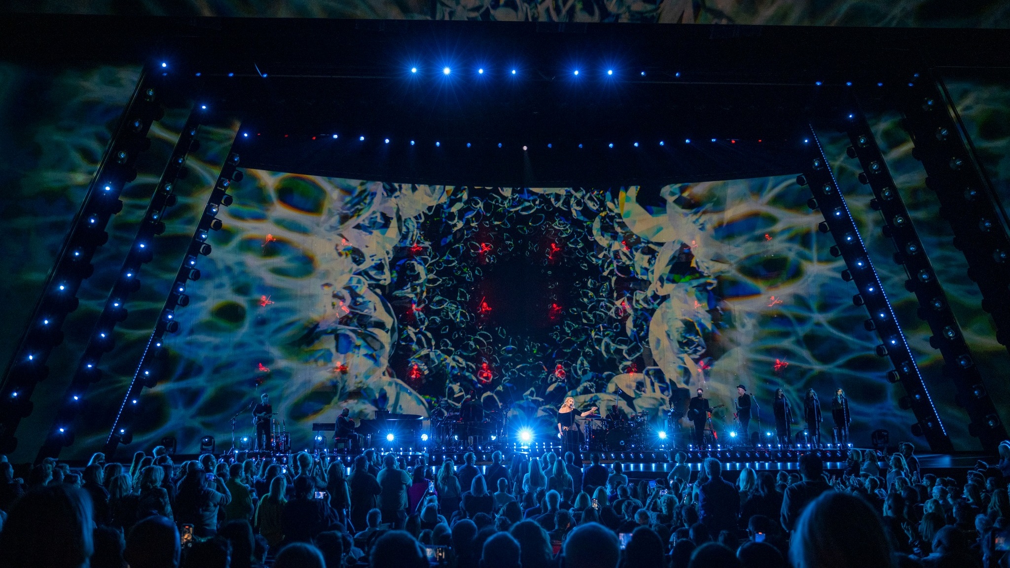 Singer Adele performing on stage lit blue with an abstract backdrop displayed on huge LED screen